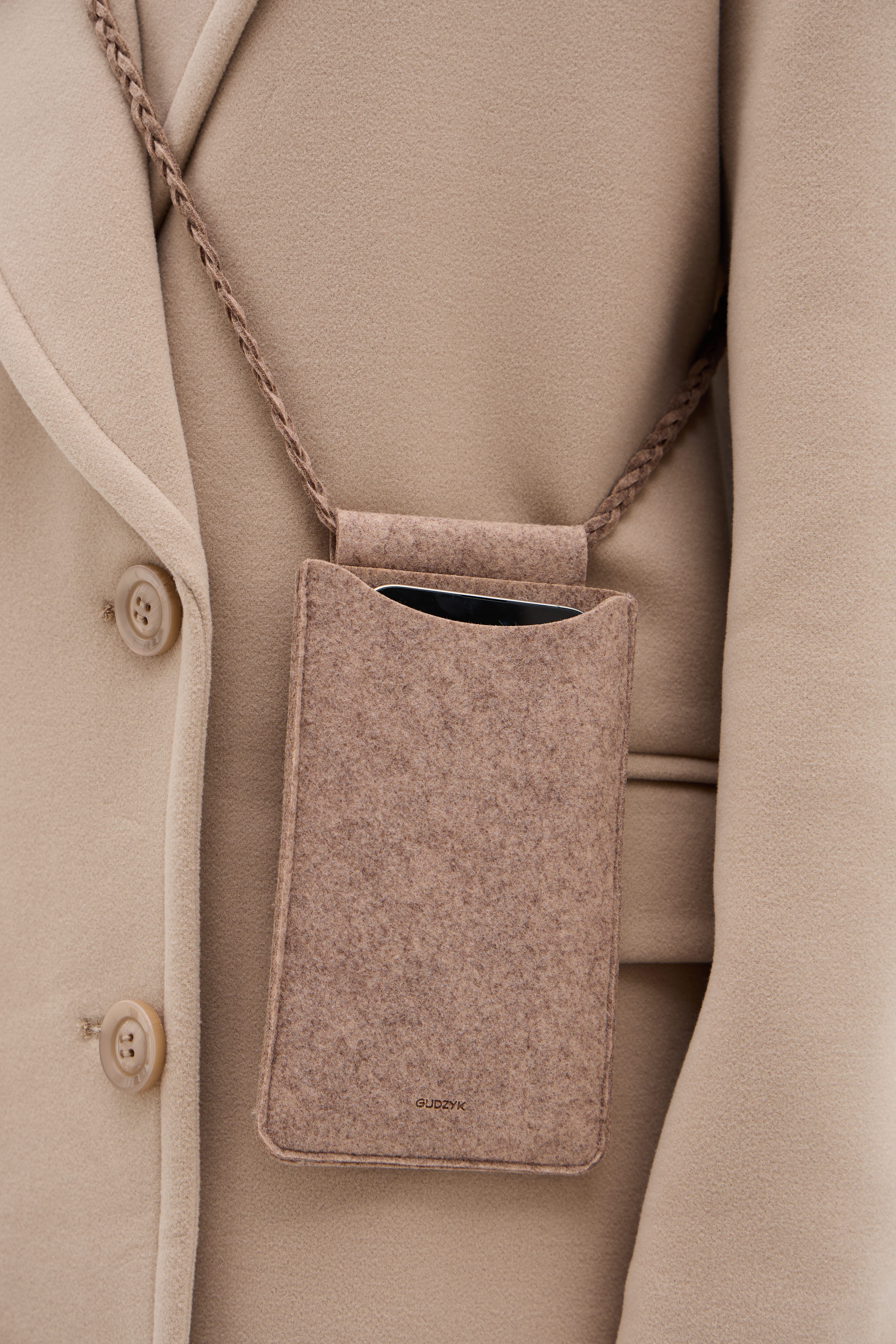 A beige shoulder bag against the backdrop of a beige coat