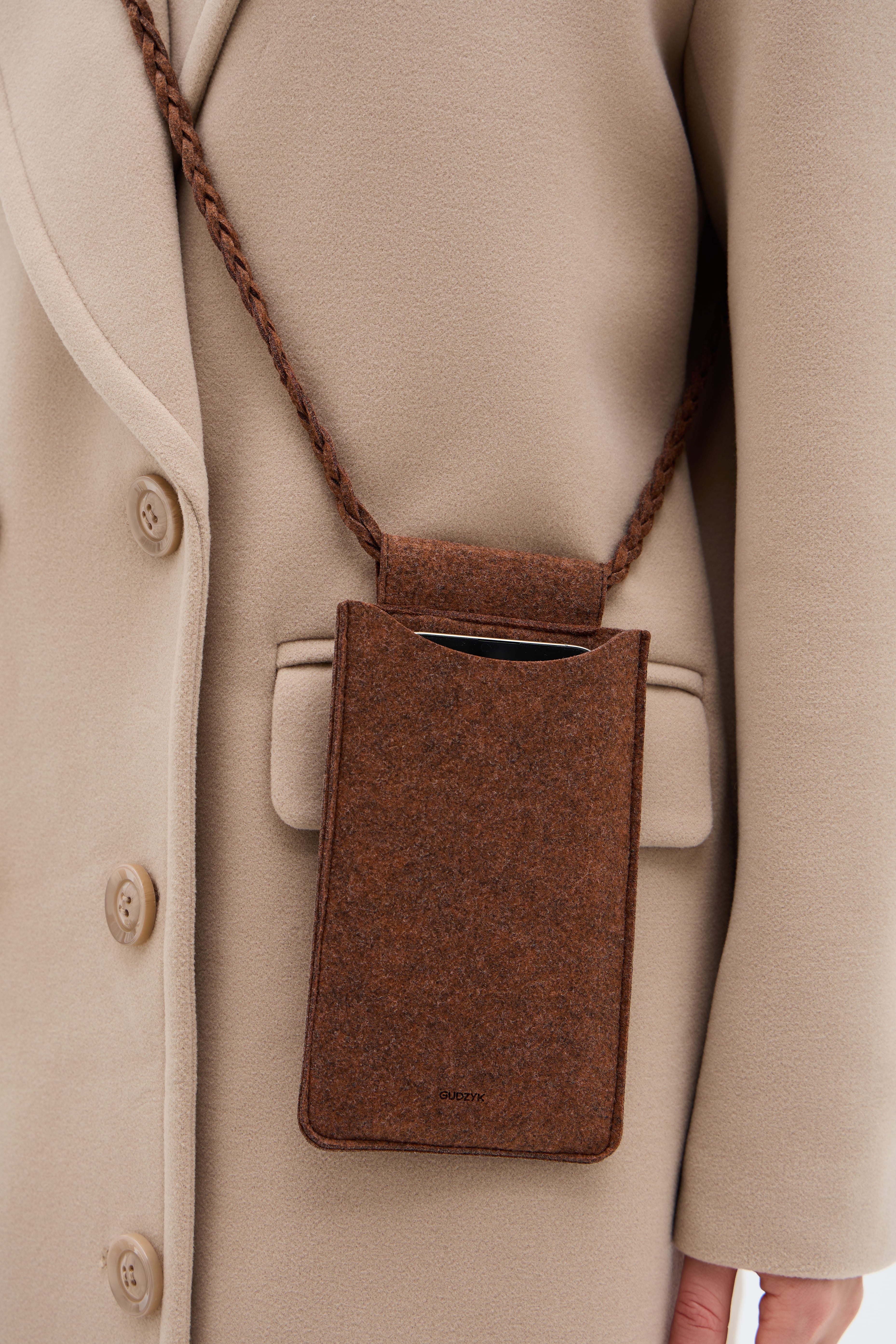 A brown shoulder bag against the backdrop of a beige coat