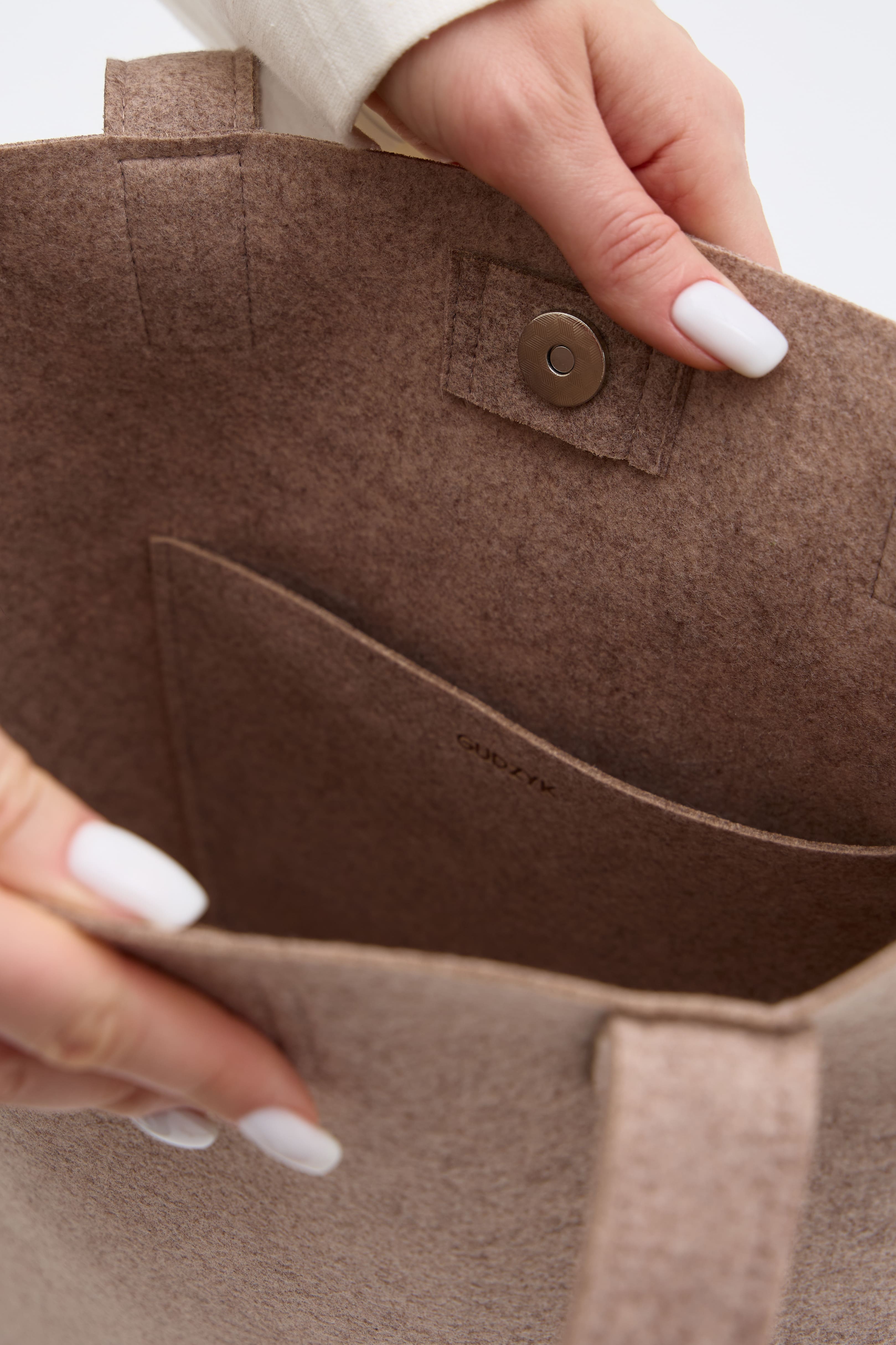 Beige fabric with a button held by hands with white nail polish on a light background