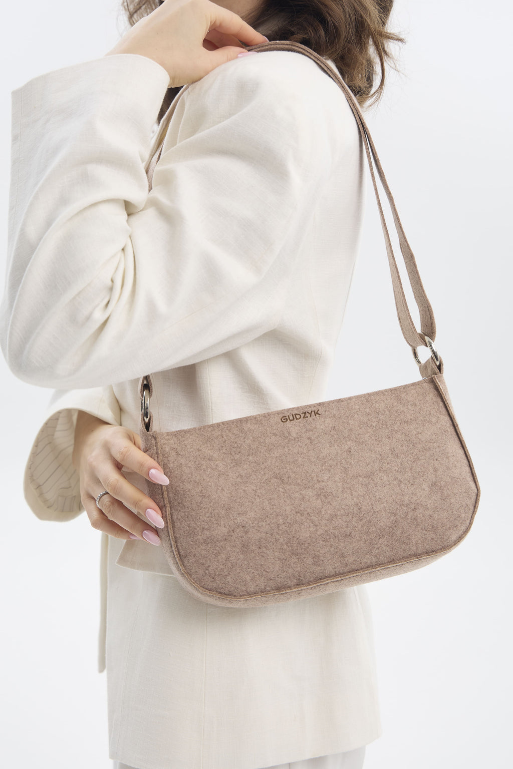 Beige handbag with a brand logo held by a person wearing a white coat on a light background