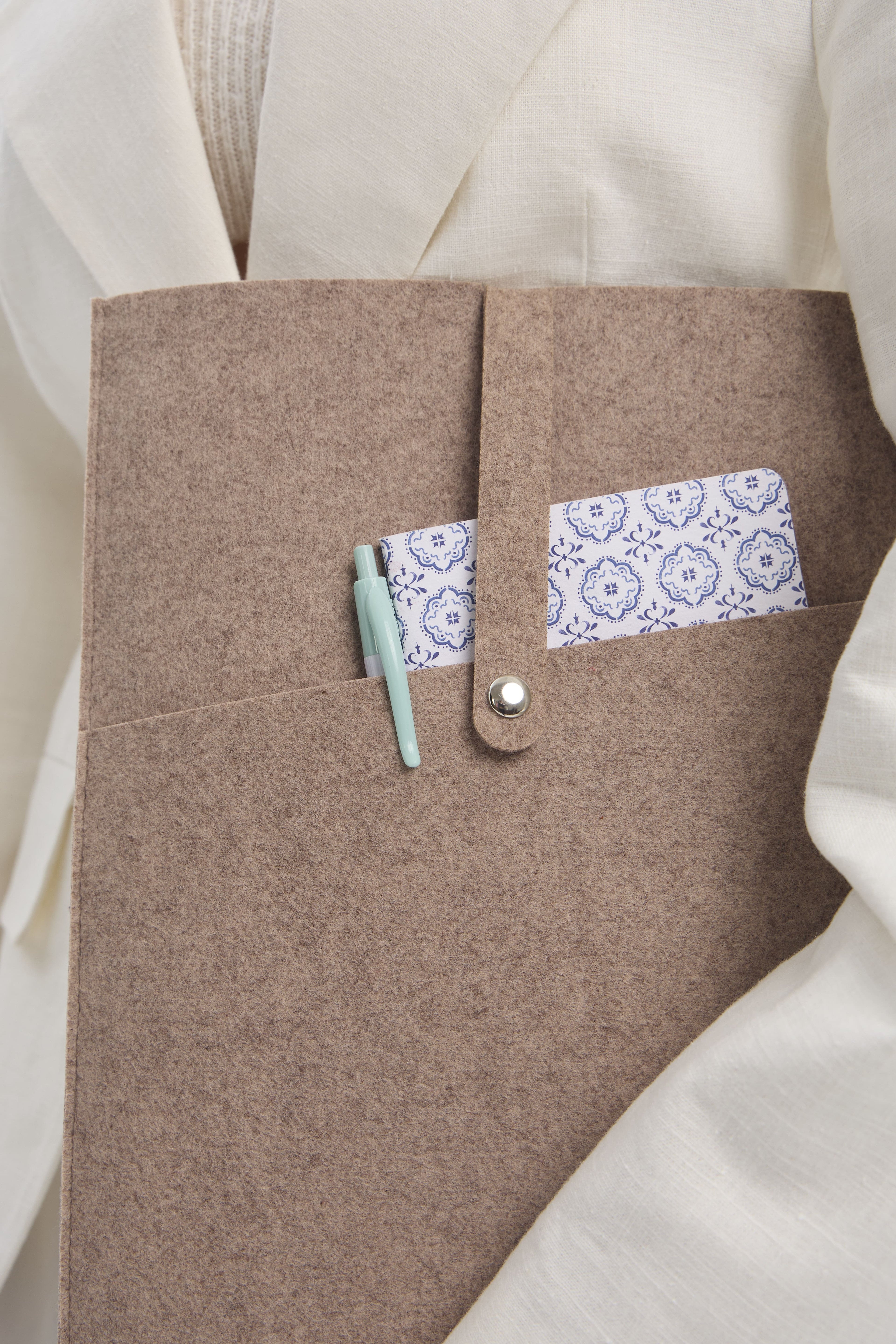 Close-up of a beige felt case with a notebook and a pen inside, on a light background.