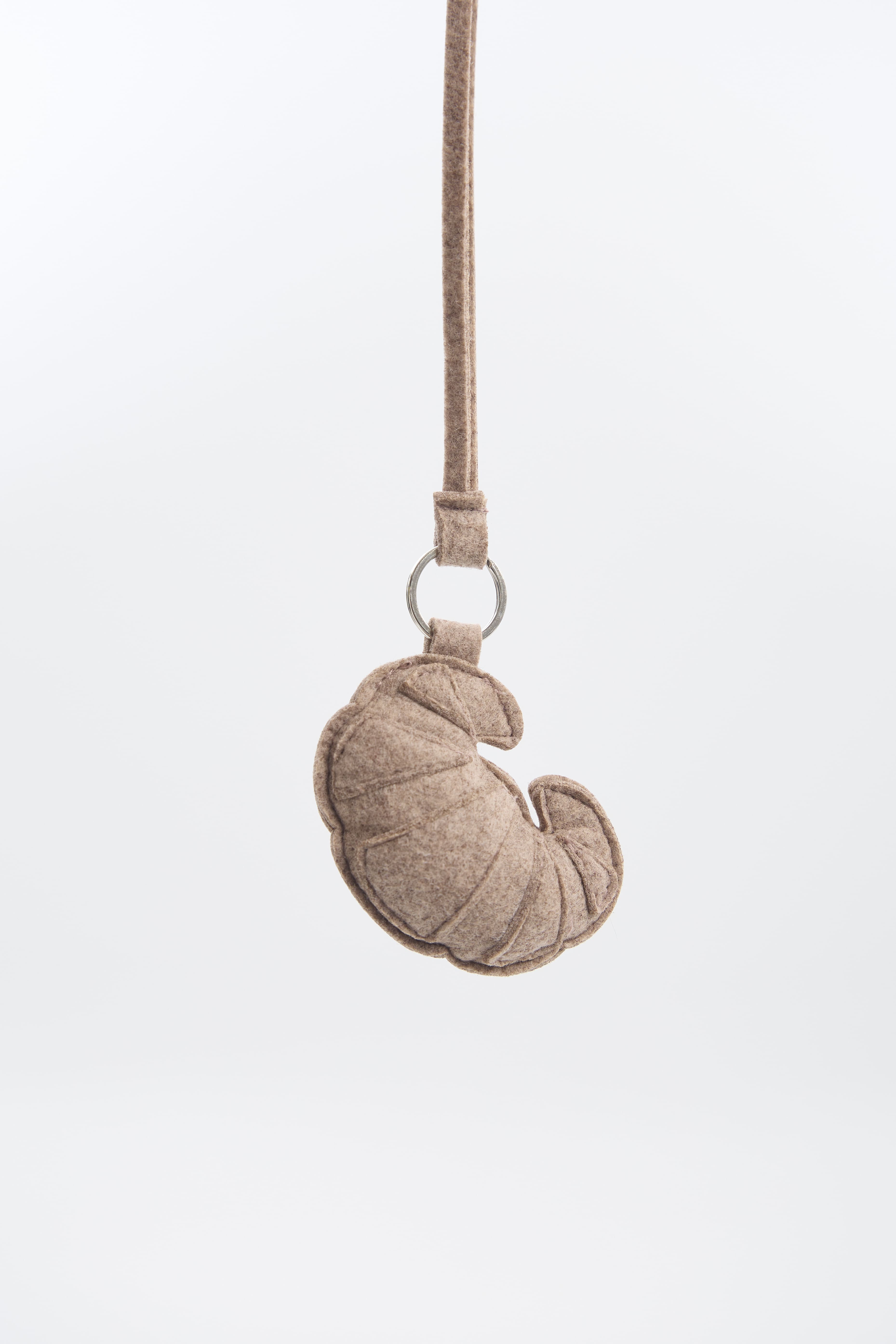 Felt beige сroissant-shaped keychain on a white background