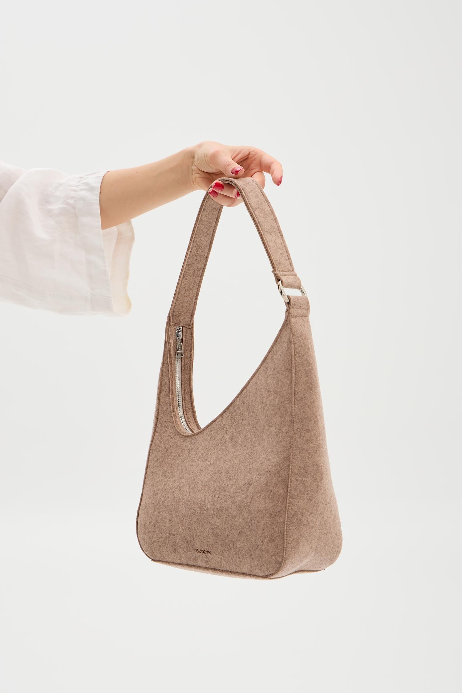Beige handbag held by a person against a white background