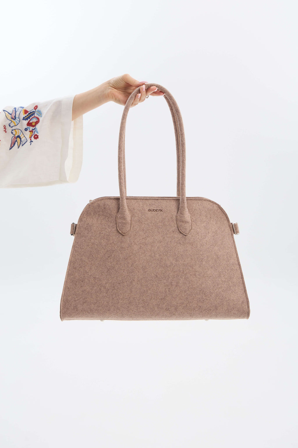 Beige handbag held by a hand against a white background