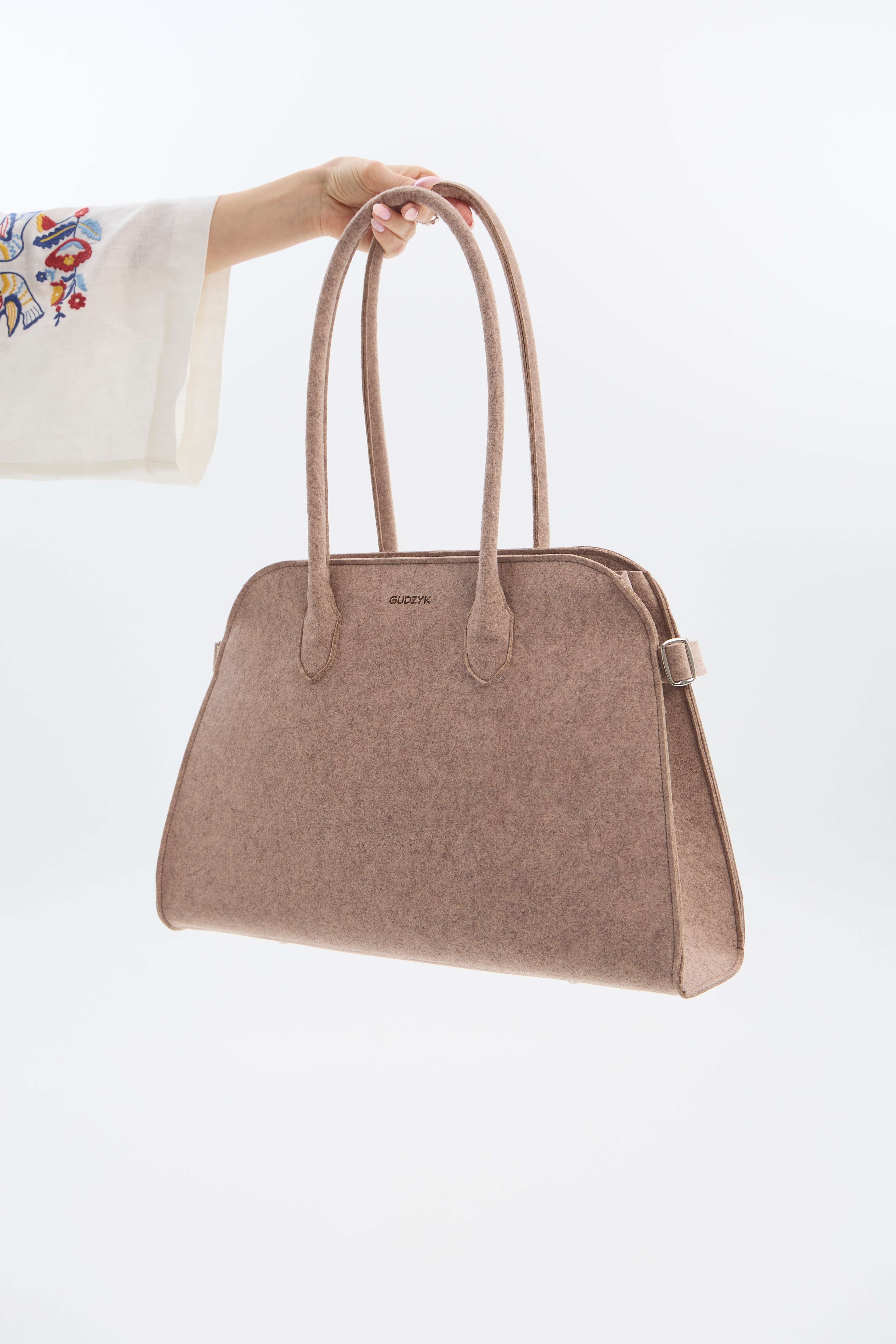 Beige handbag held by a person with a white background