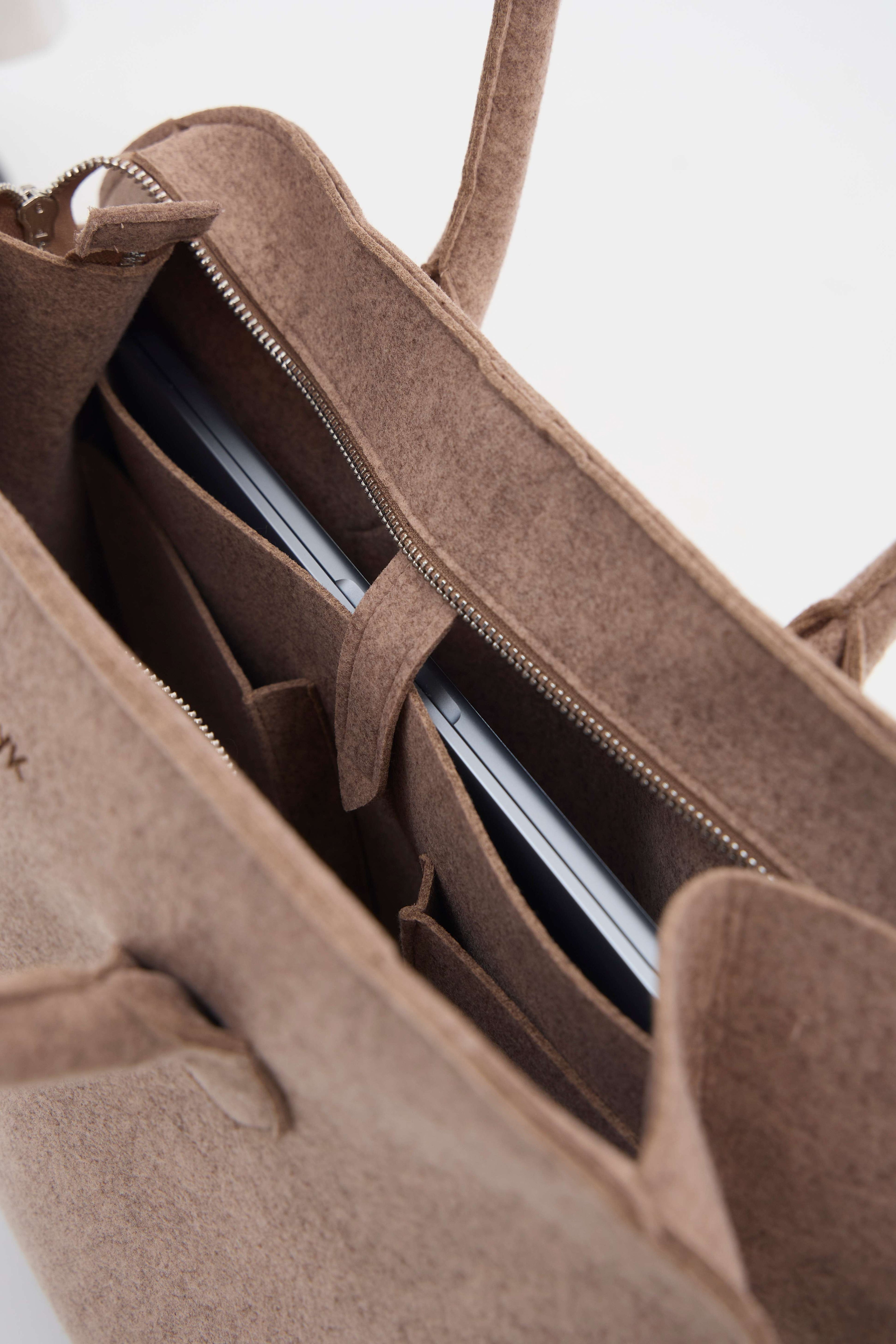 Beige suede handbag with a laptop inside on a white background