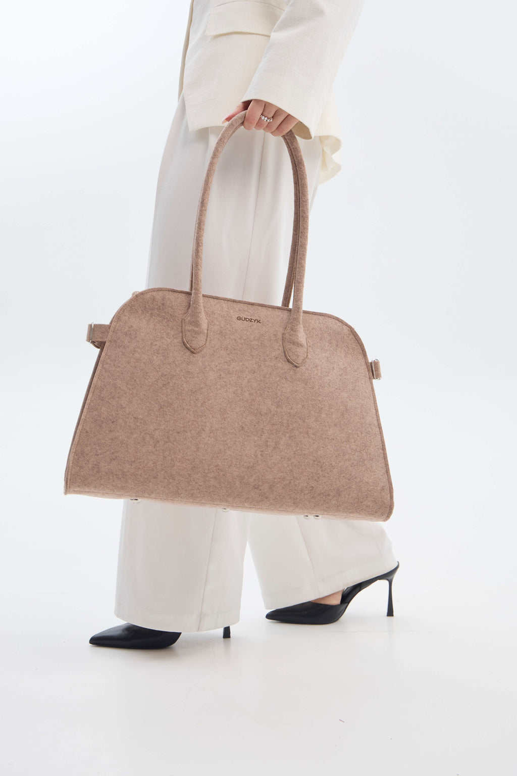 Beige handbag held by a person wearing a white outfit on a white background