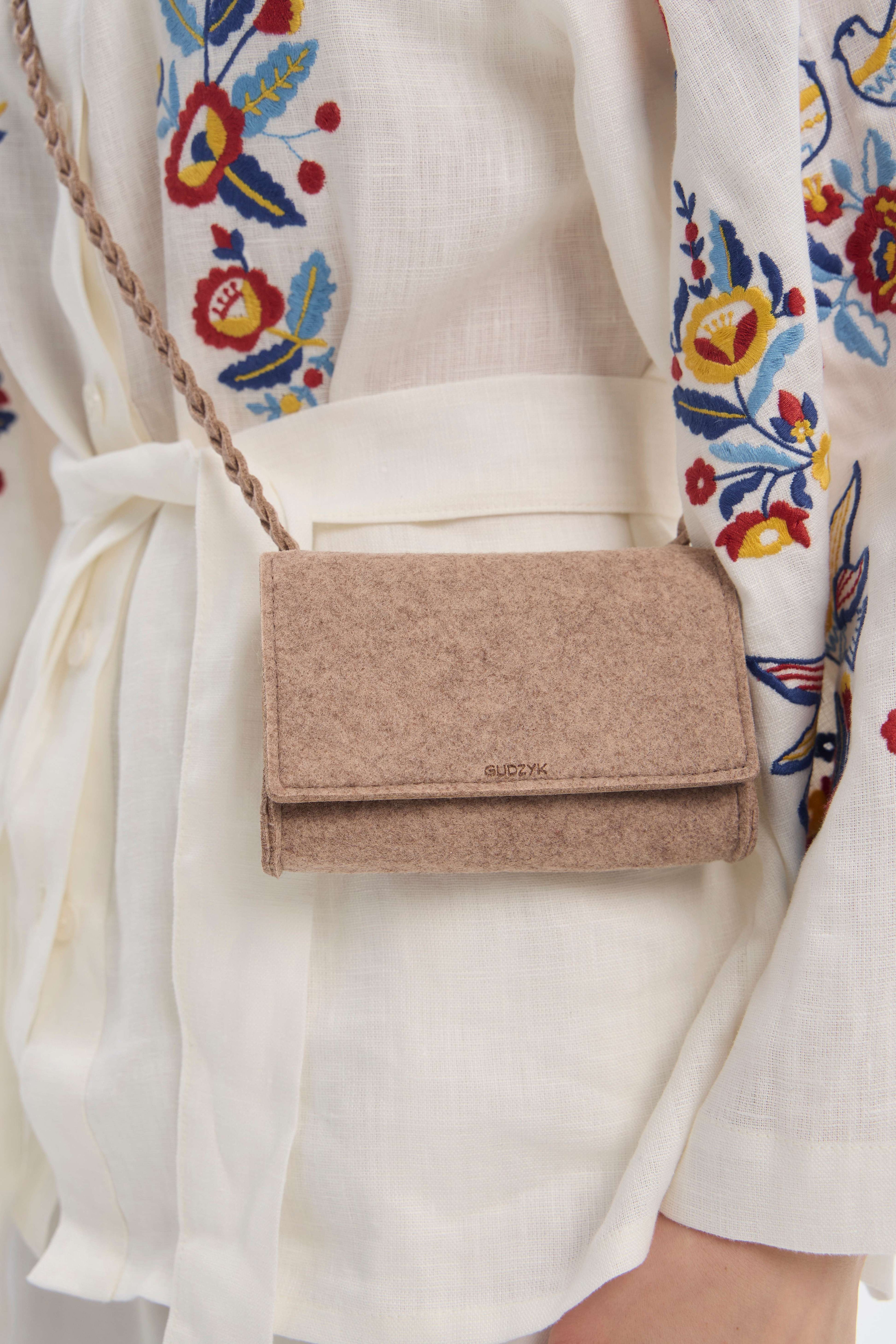 Beige felt mini crossbody bag worn by a person with a colorful floral-patterned garment.