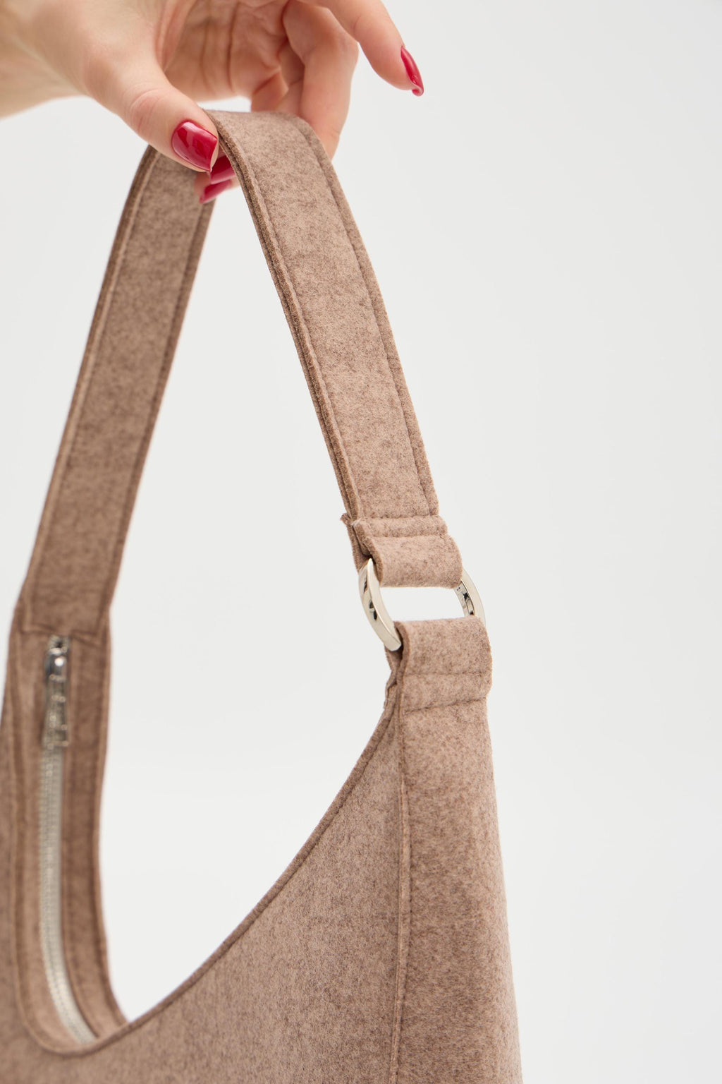 Beige shoulder bag held by a hand with red nail polish on a light gray background