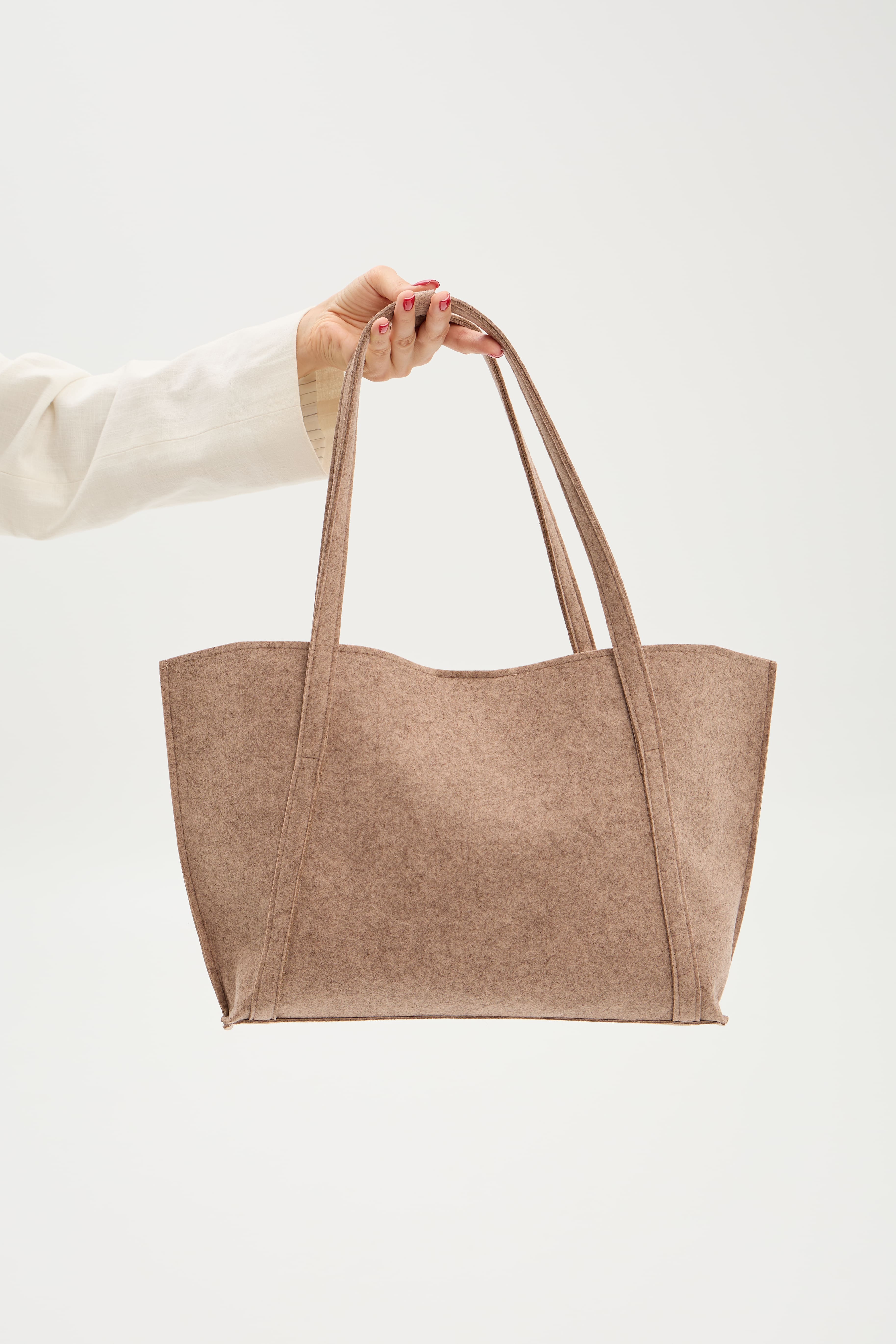 Beige tote bag held by a person against a white background