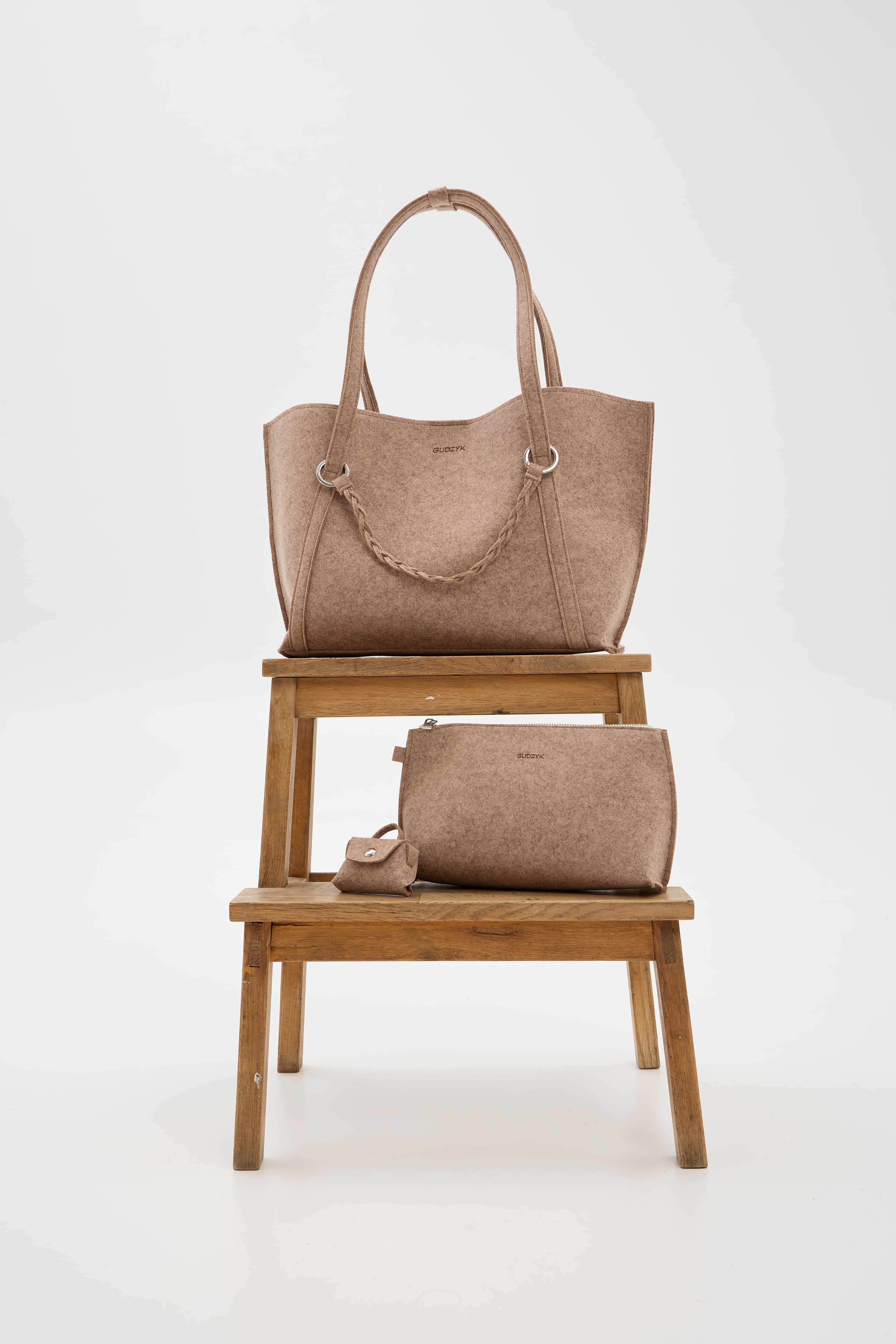 Beige handbag and smaller pouch on a wooden stool against a white background