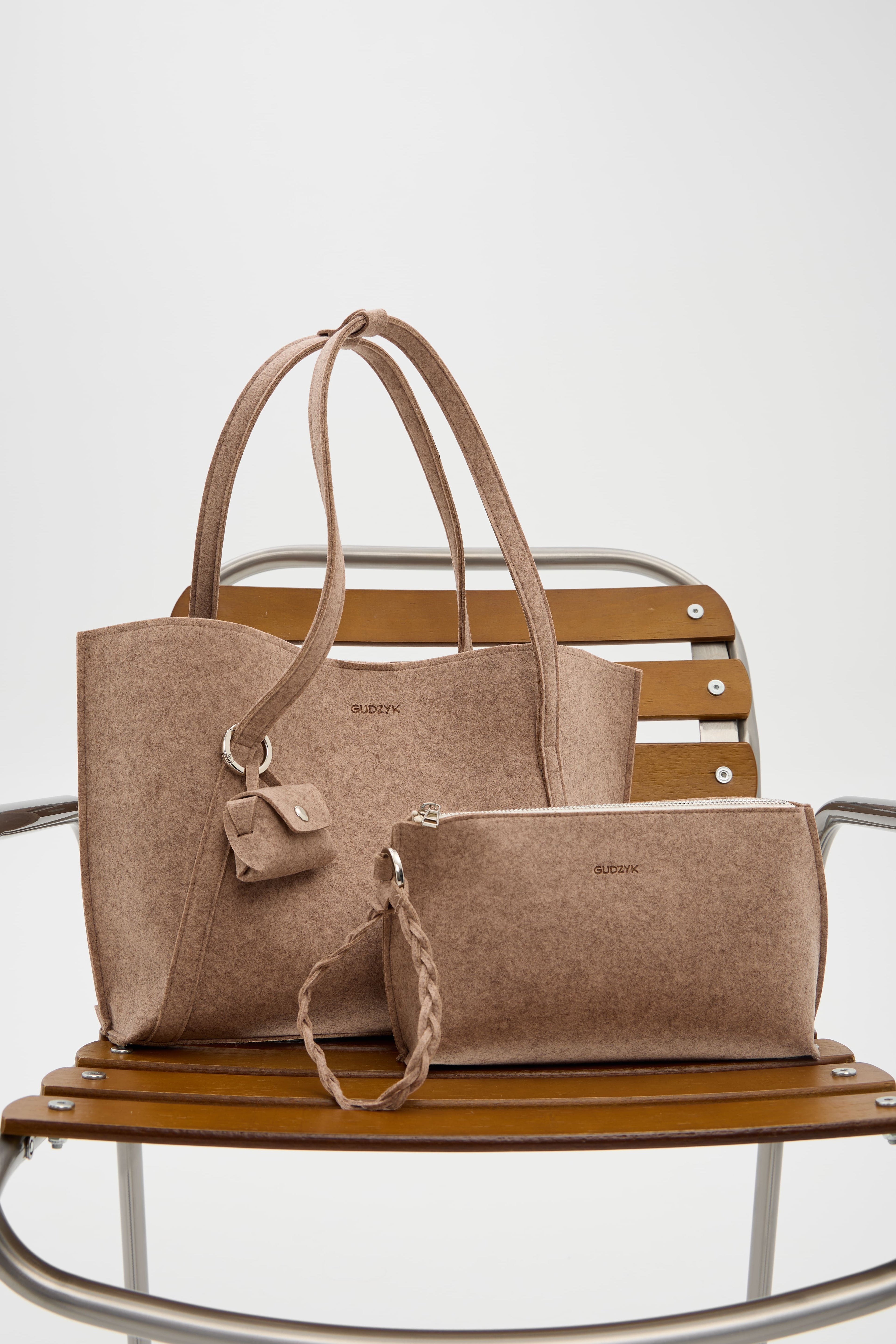 Beige handbag and matching pouch on a wooden chair with a white background