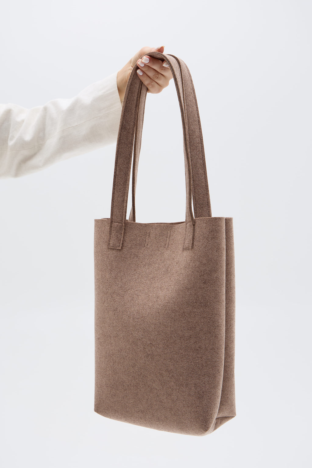 Beige tote bag held by a person against a white background