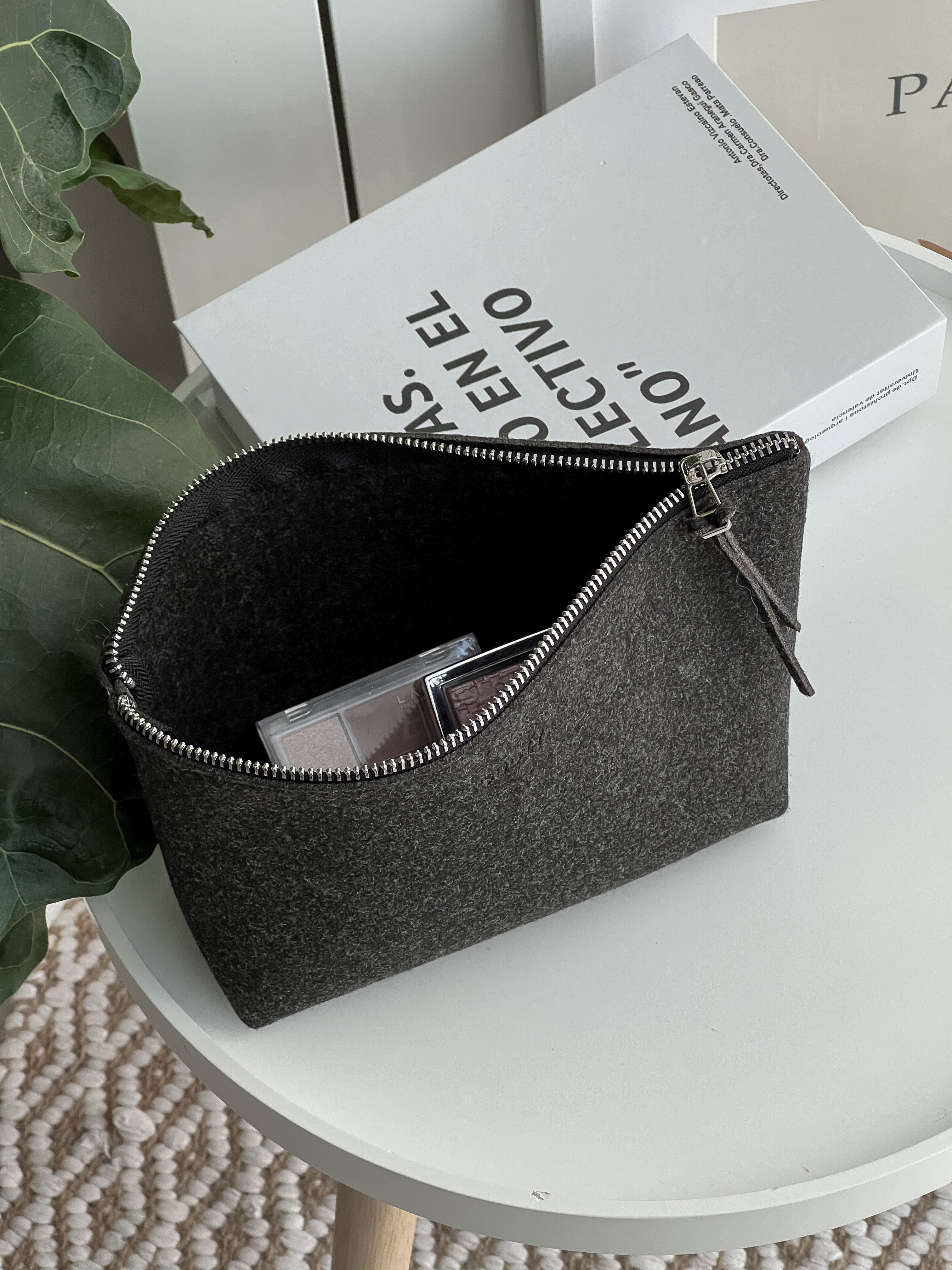 Black zippered pouch on a white surface with a book in the background