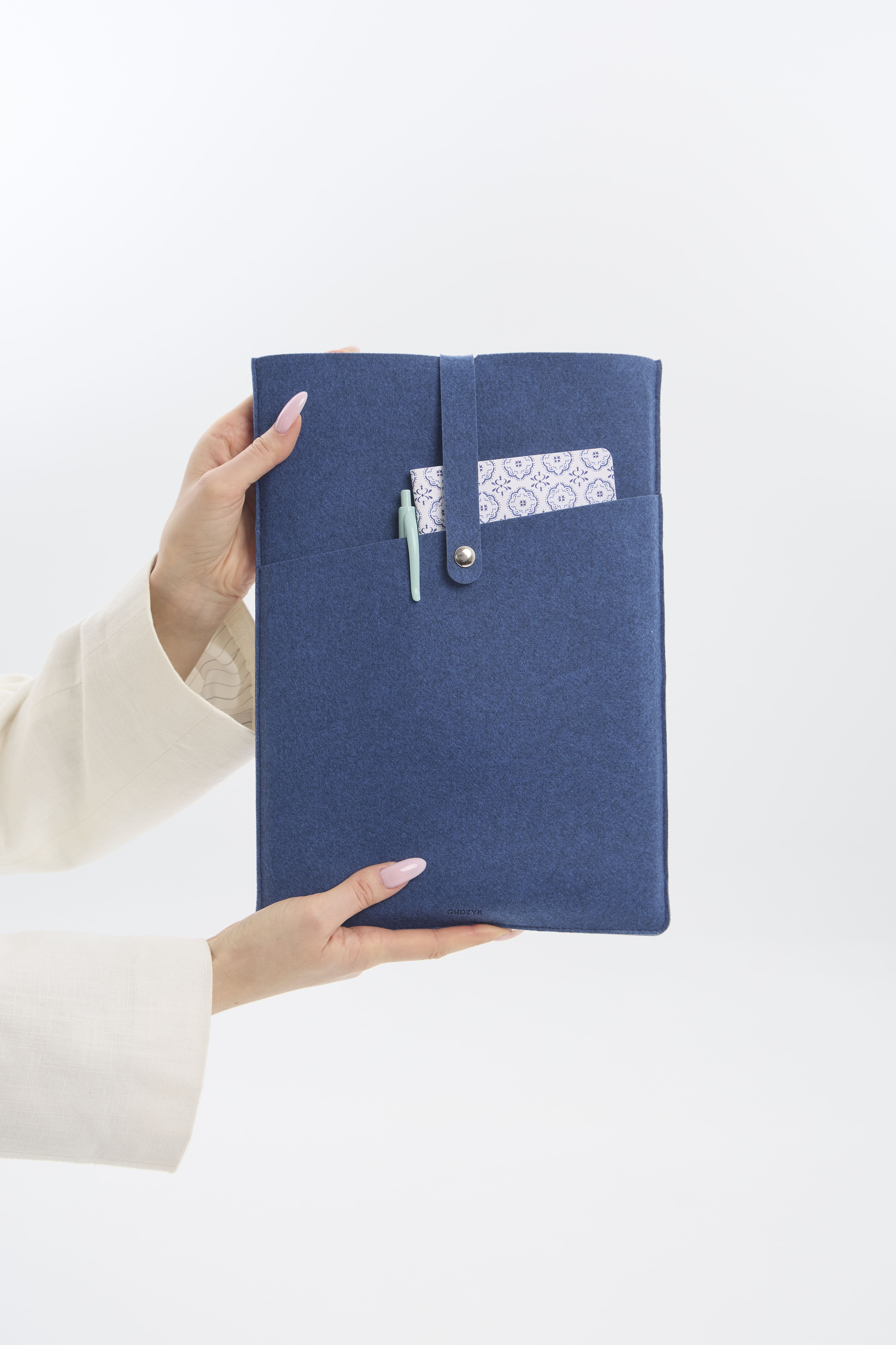 Hand holding a blue felt case with a button and pocket on a white background