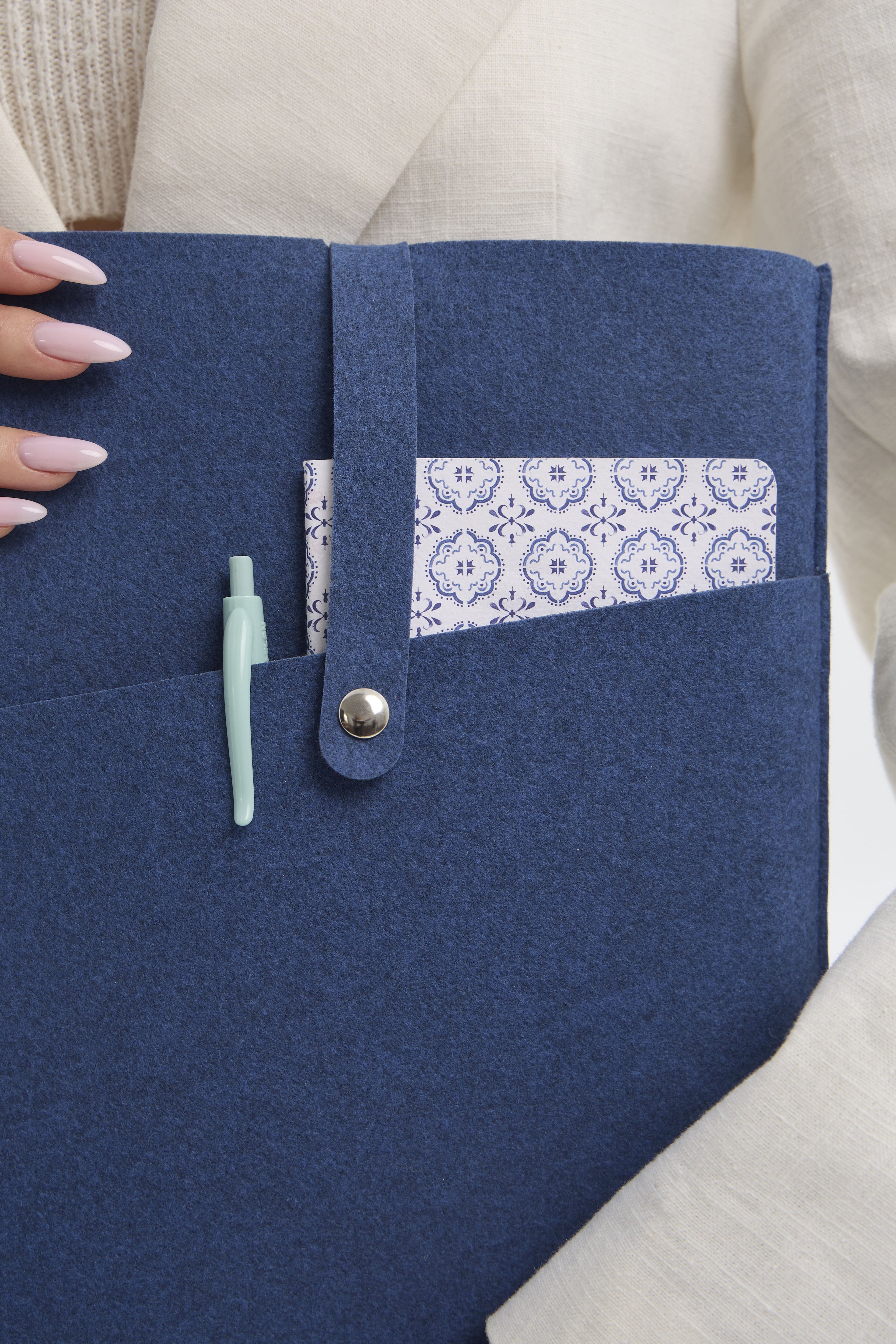 A blue case with a pocket for a notebook, held by a person wearing a beige outfit.