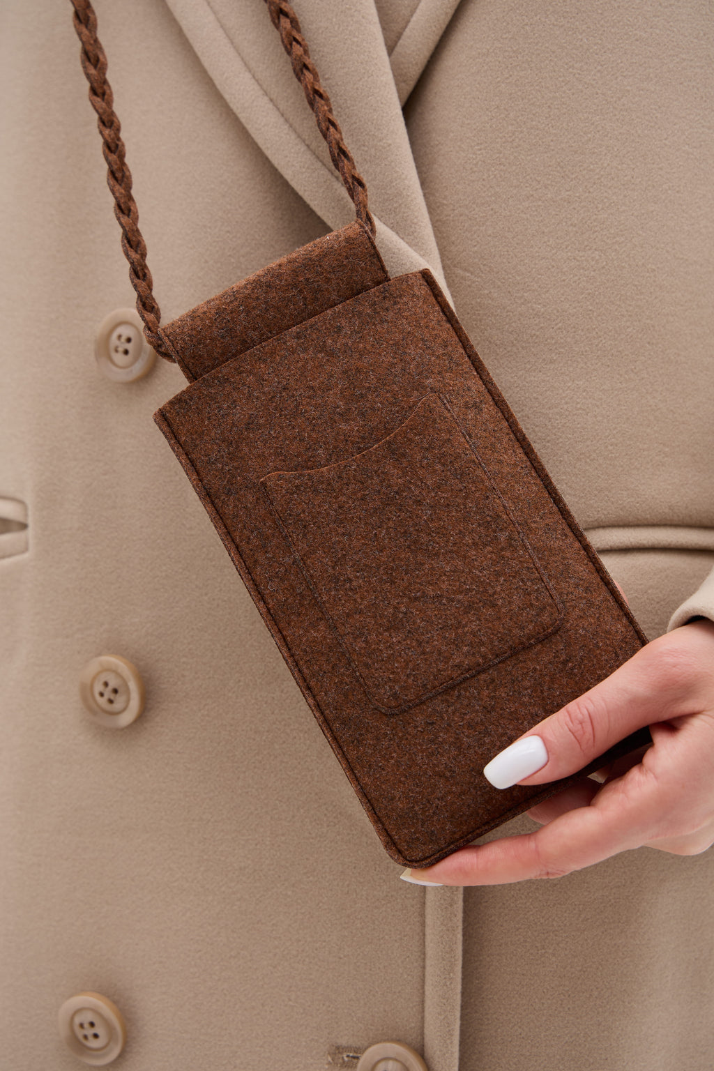 Brown ecofelt crossbody bag held by a person wearing a beige coat.