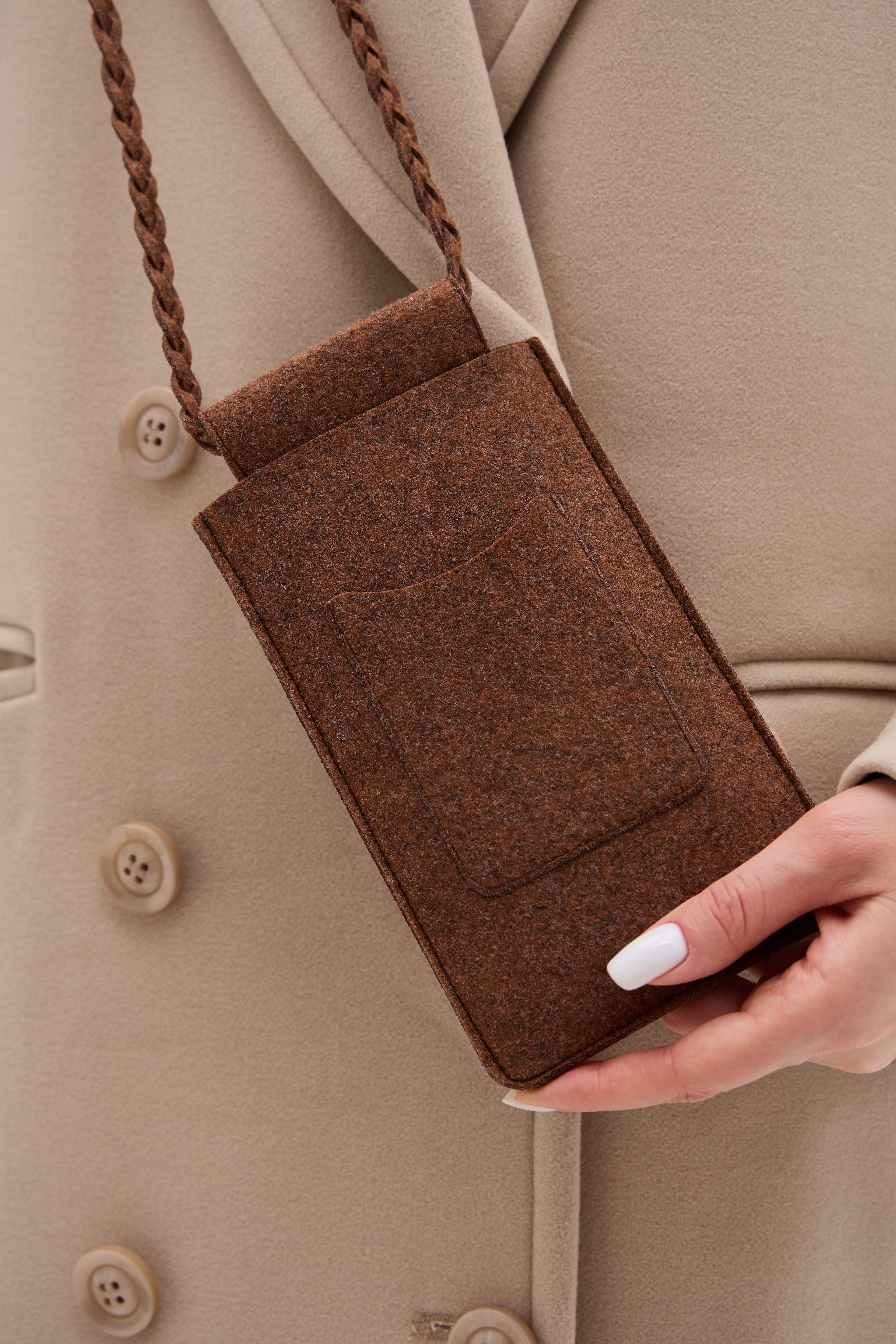 Brown ecofelt crossbody bag held by a person wearing a beige coat.