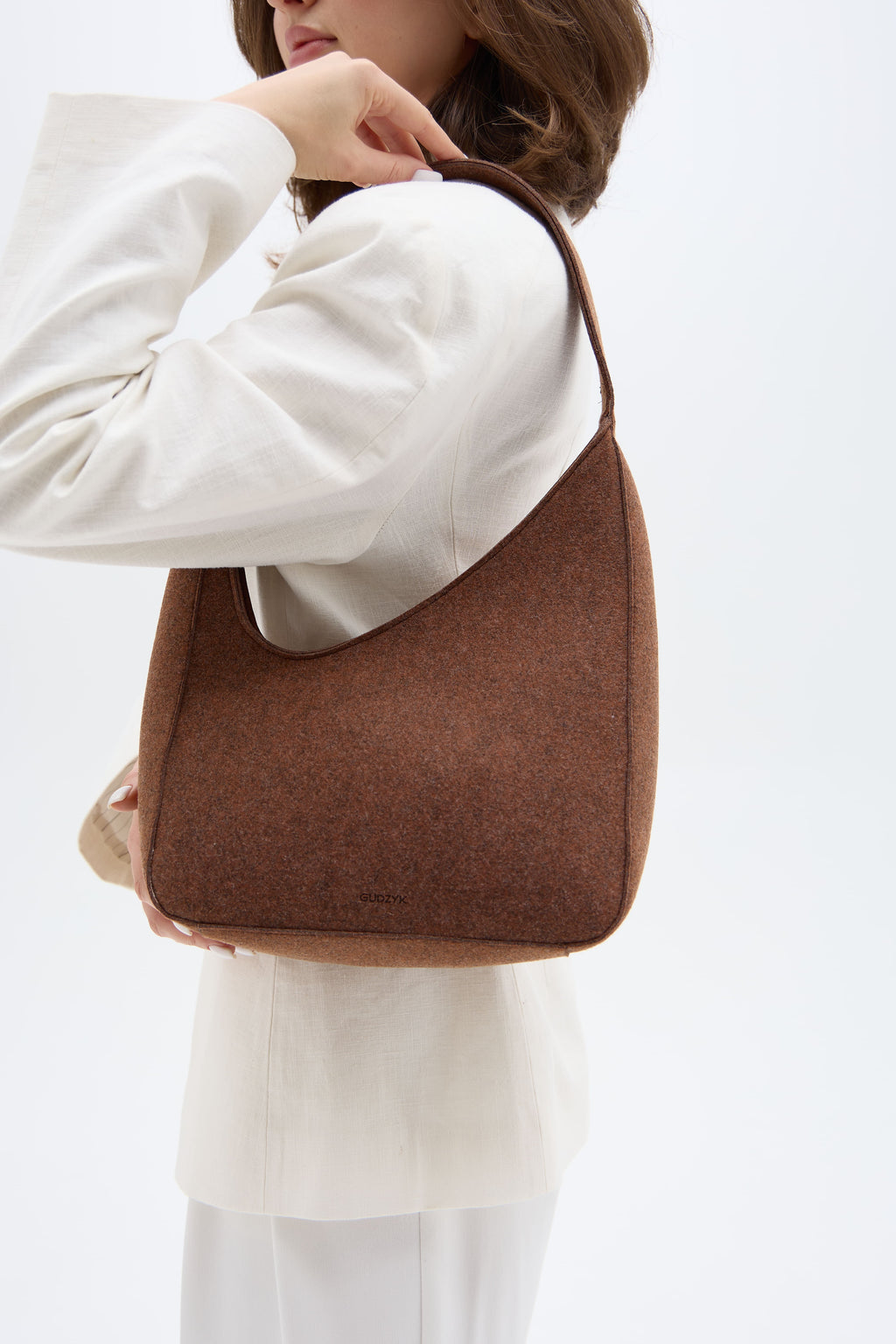 Brown shoulder bag held by a person wearing a white outfit on a light background