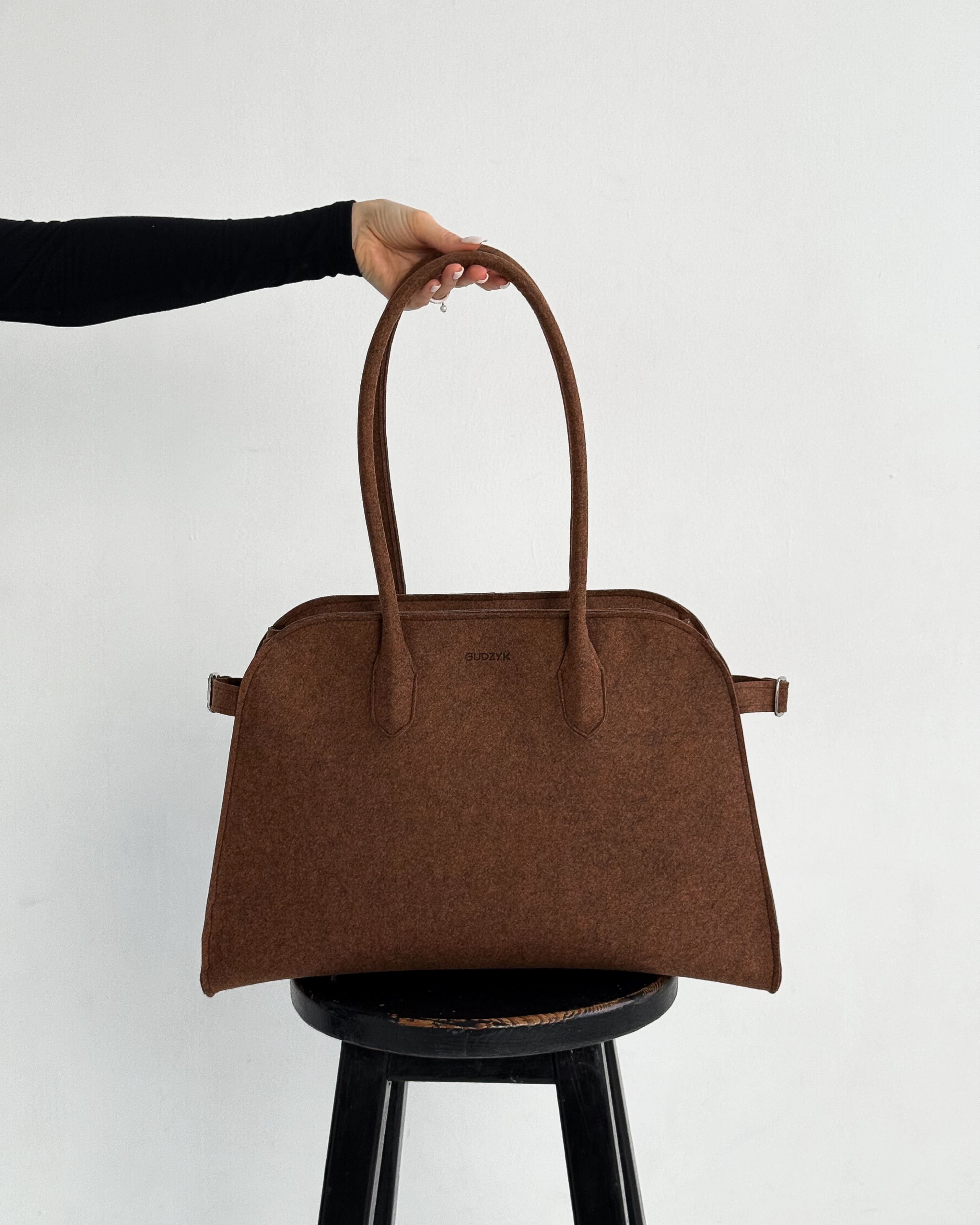 Brown handbag held above a black stool against a white background