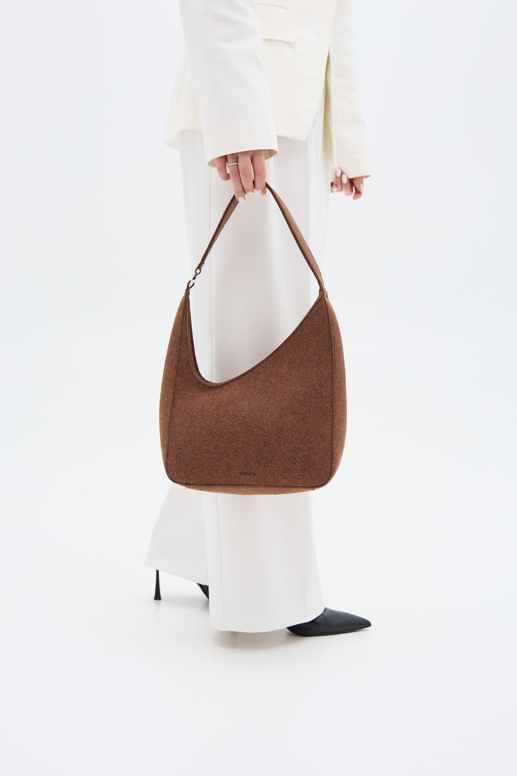 Brown shoulder bag held by a person wearing a white outfit on a white background