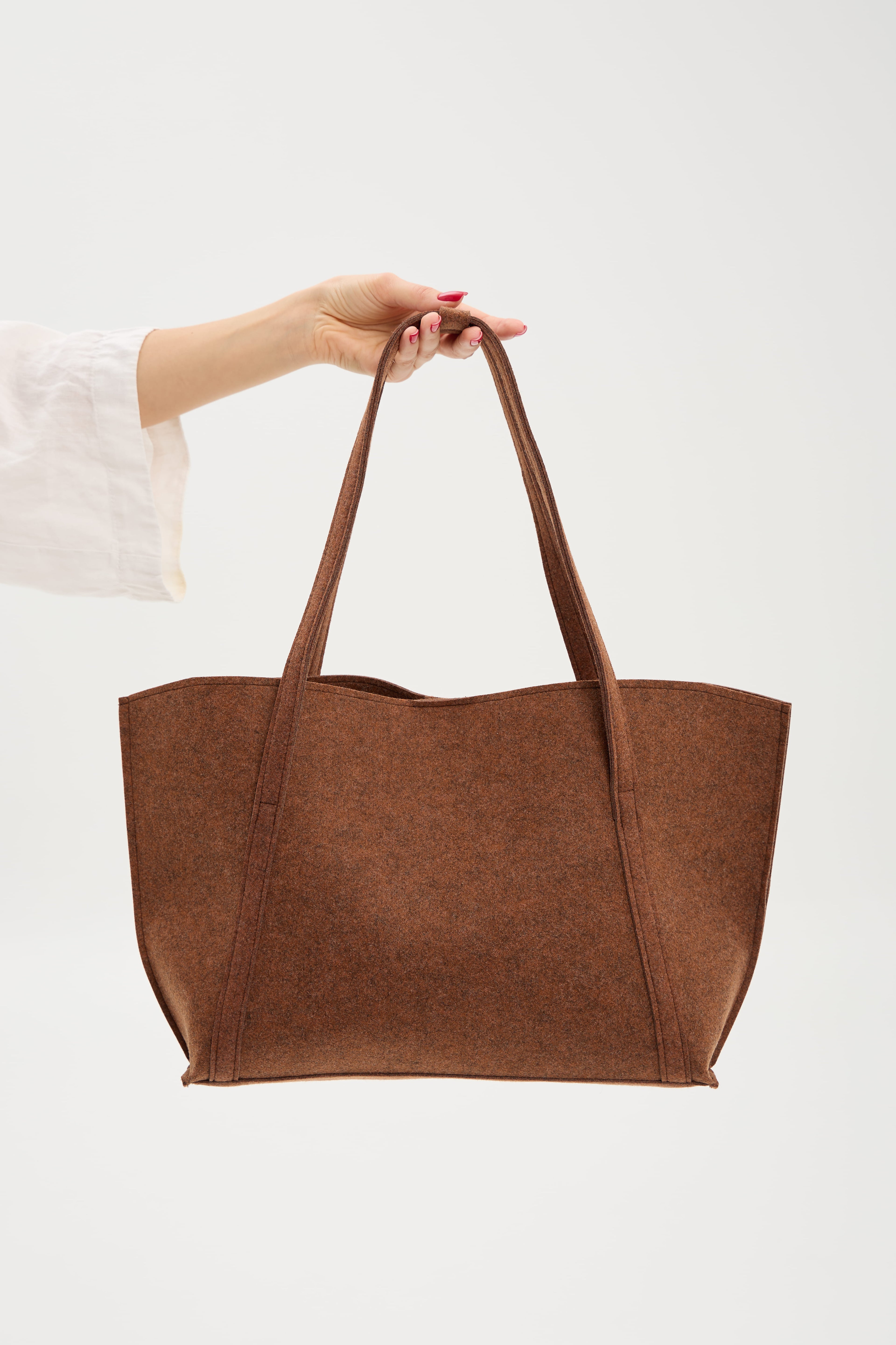 Brown tote bag held by a hand on a white background