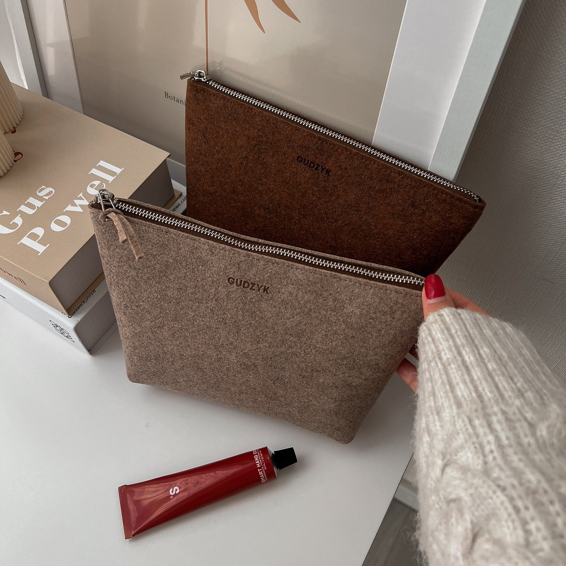 Brown pouches with 'GUDZYK' branding on a white surface with a tube of red cream.