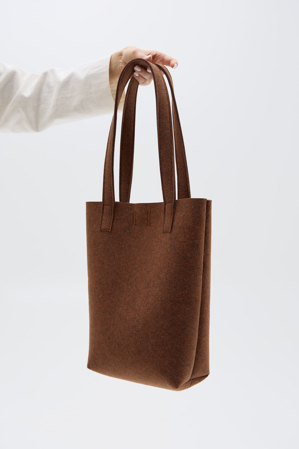 Brown tote bag held by a person against a white background