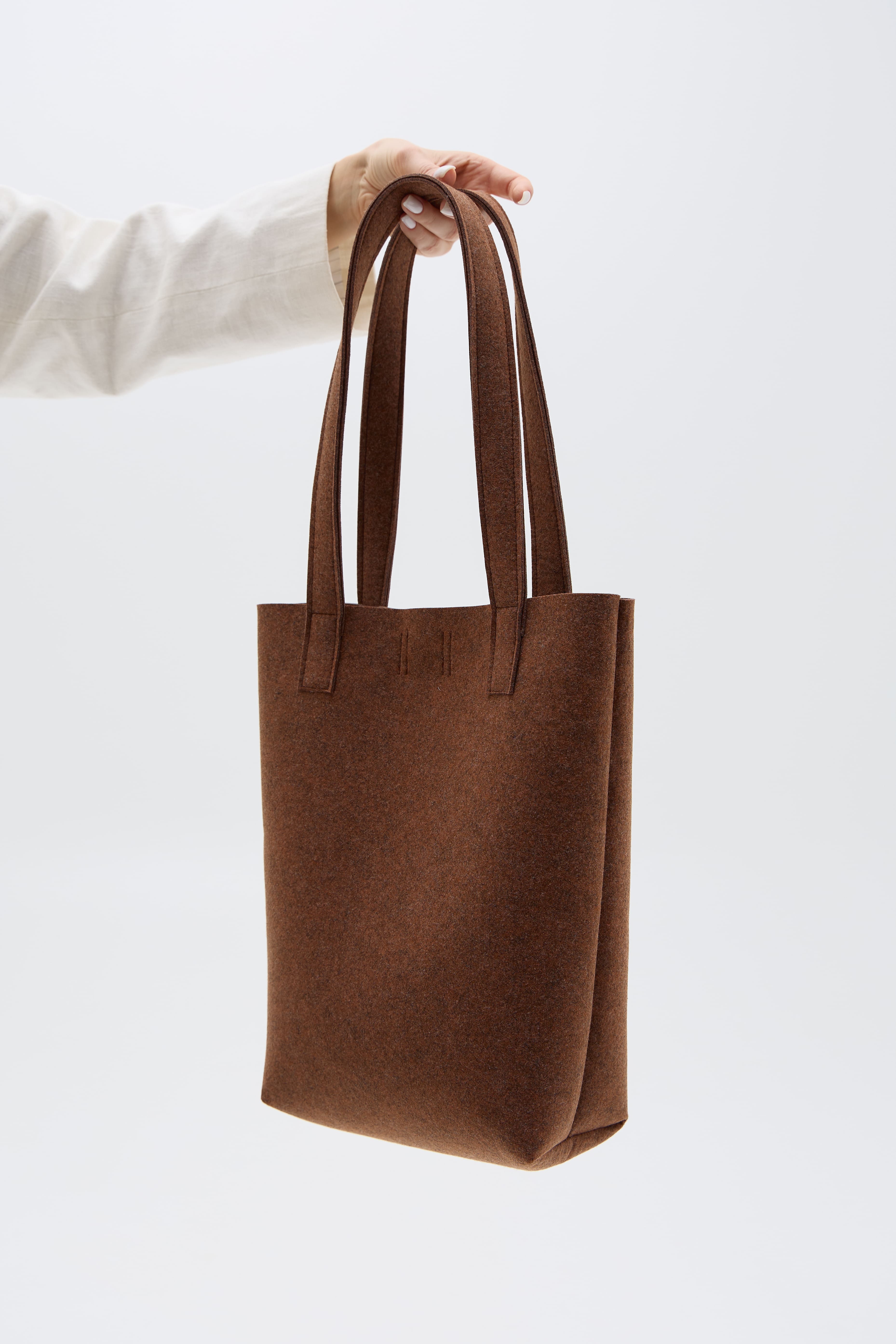 Brown tote bag held by a person against a white background