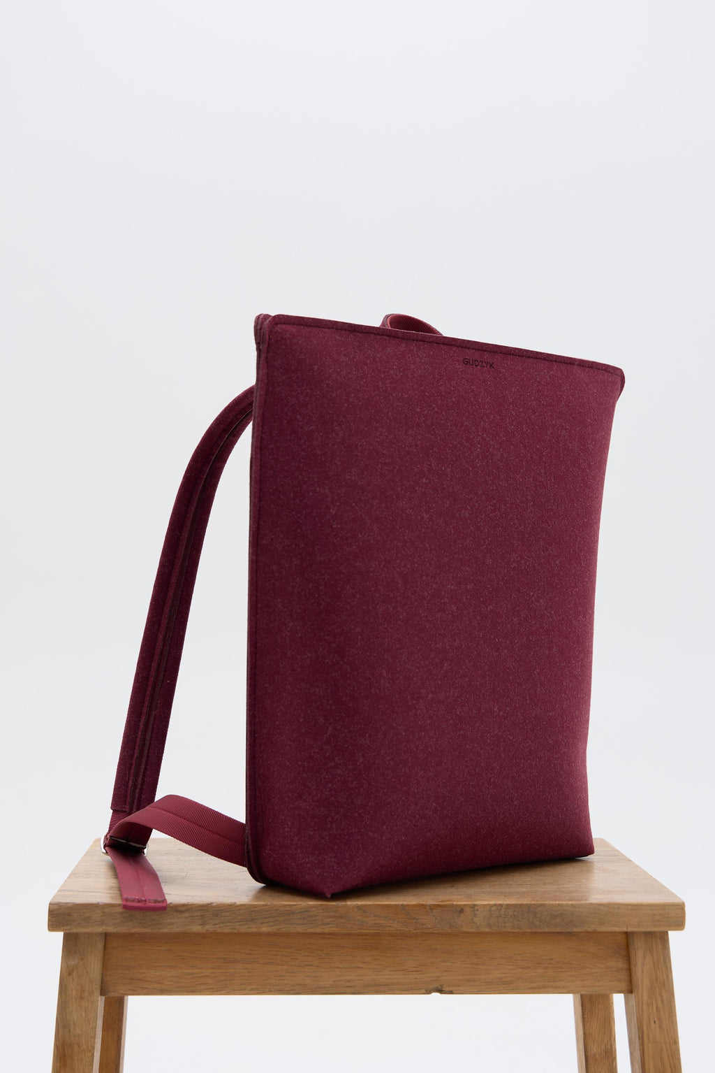Burgundy backpack on a wooden stool with a white background