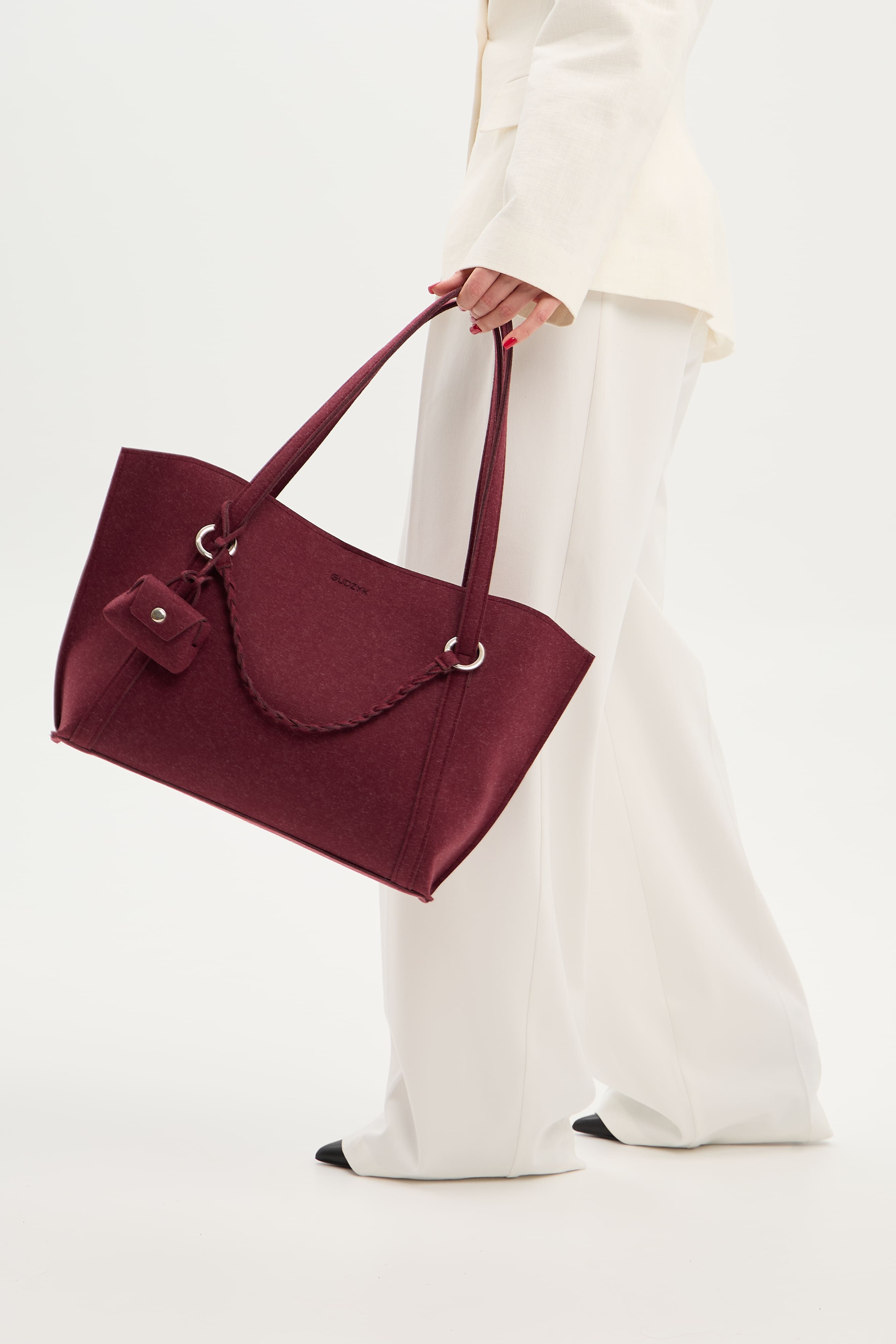 Burgundy handbag held by a person wearing white pants on a light background