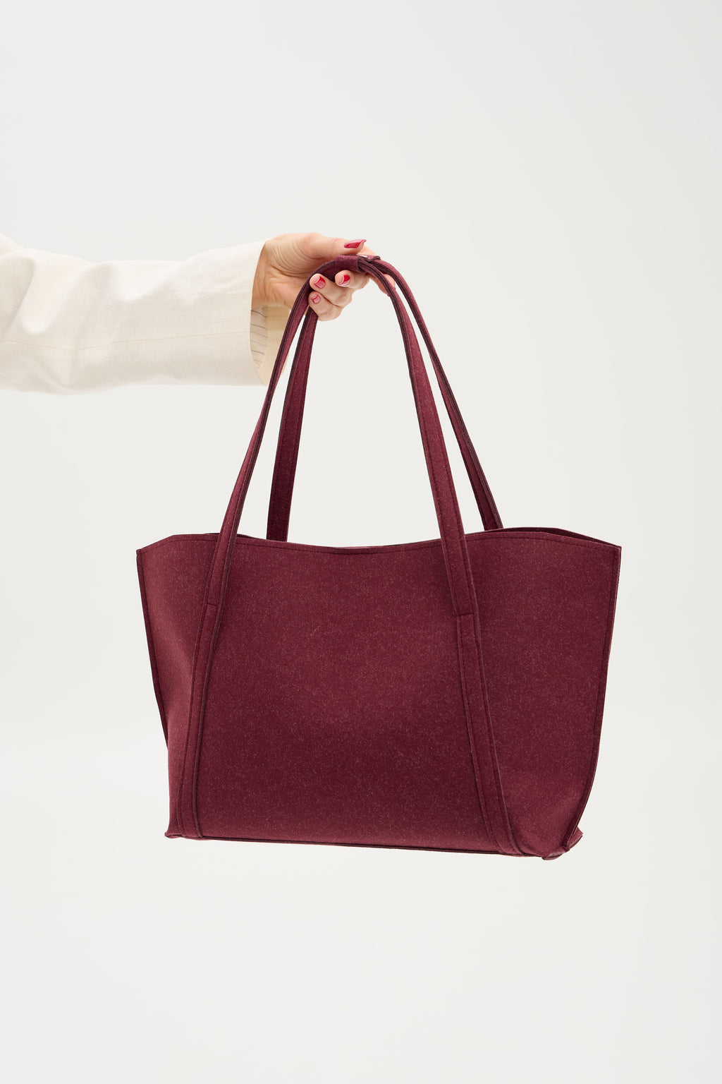 Burgundy tote bag held by a hand on a white background