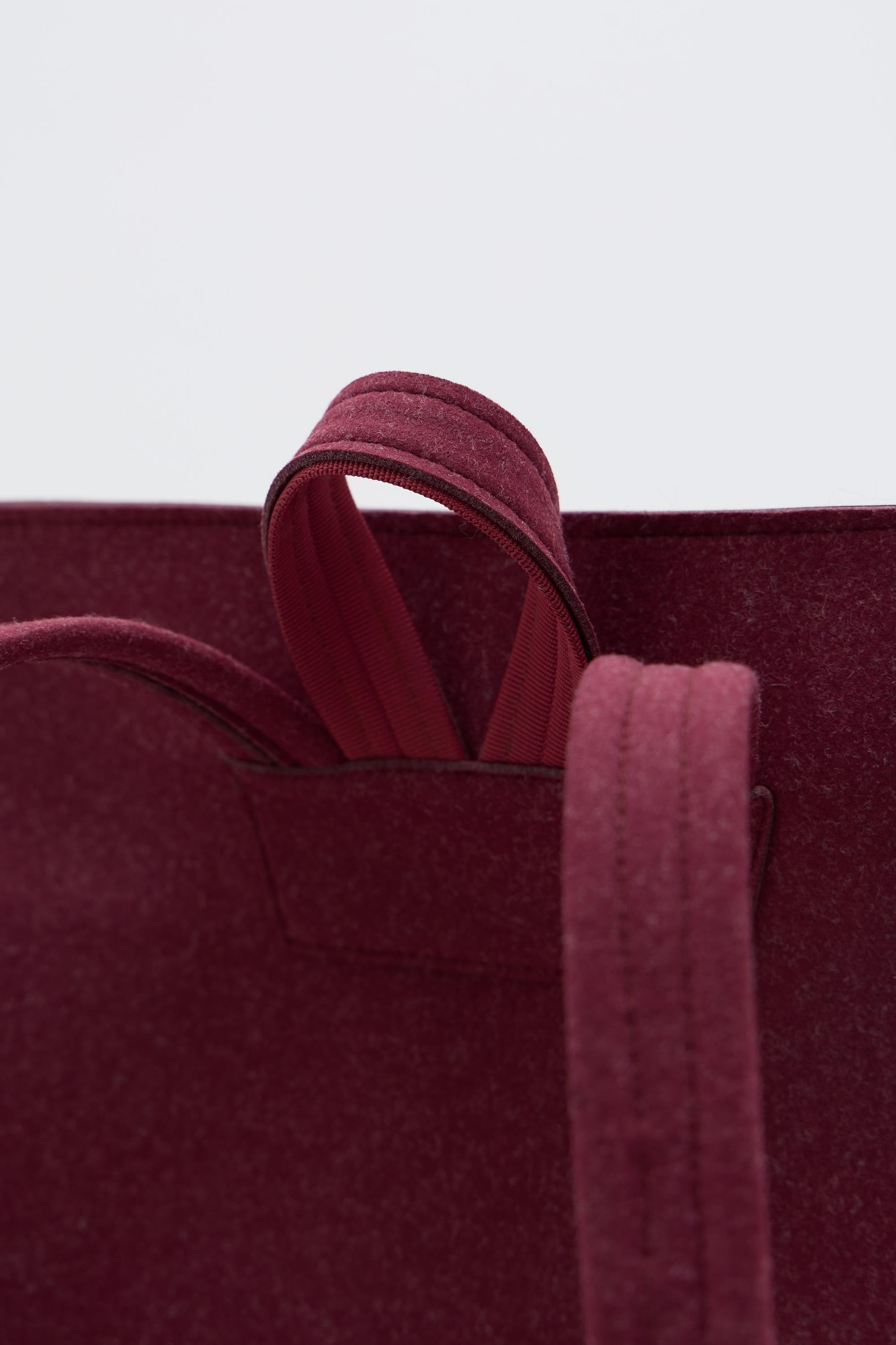 Close-up of a burgundy backpack with handles on a light gray background