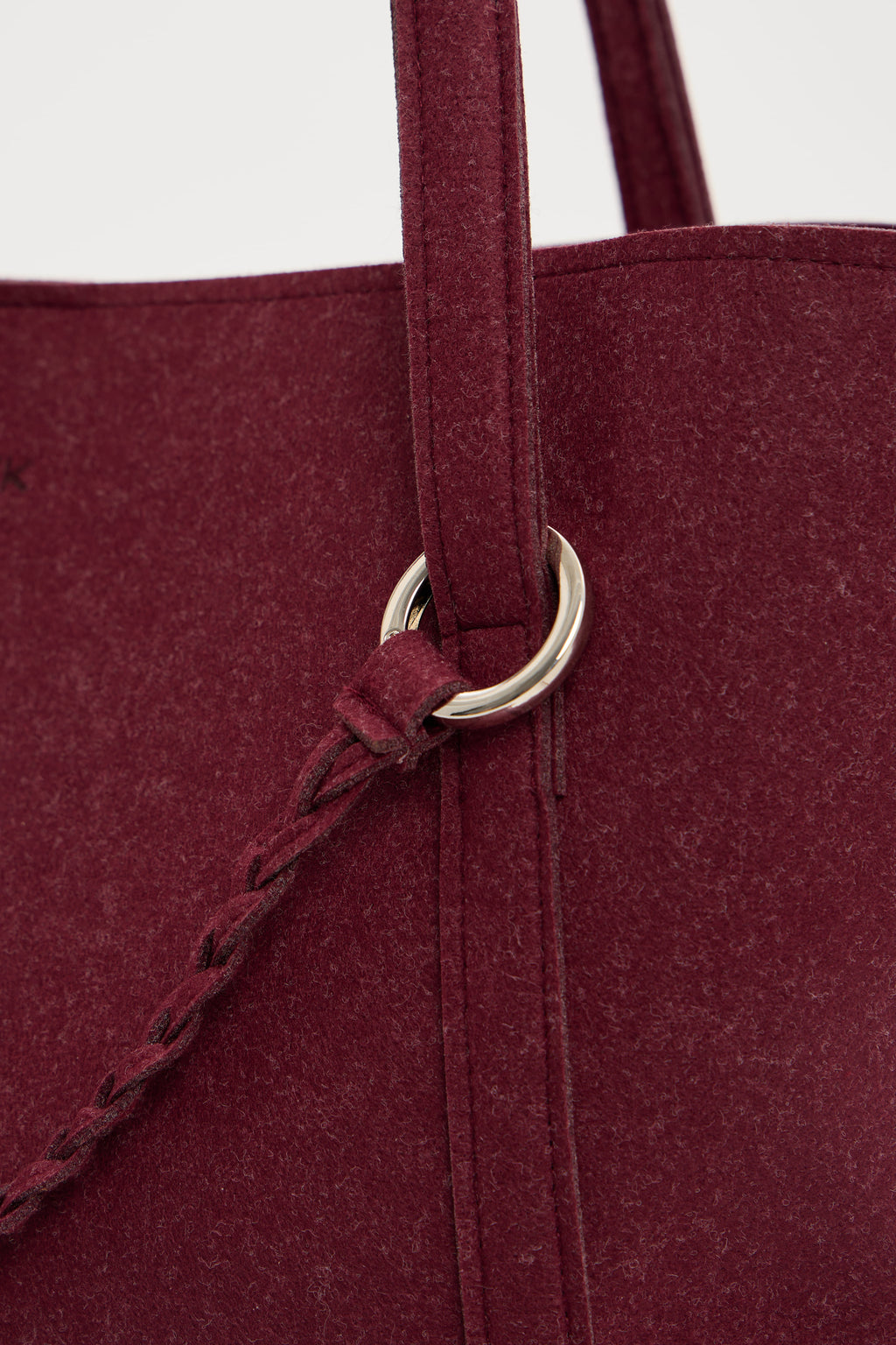 Close-up of a burgundy tote bag with a metal ring handle on a white background