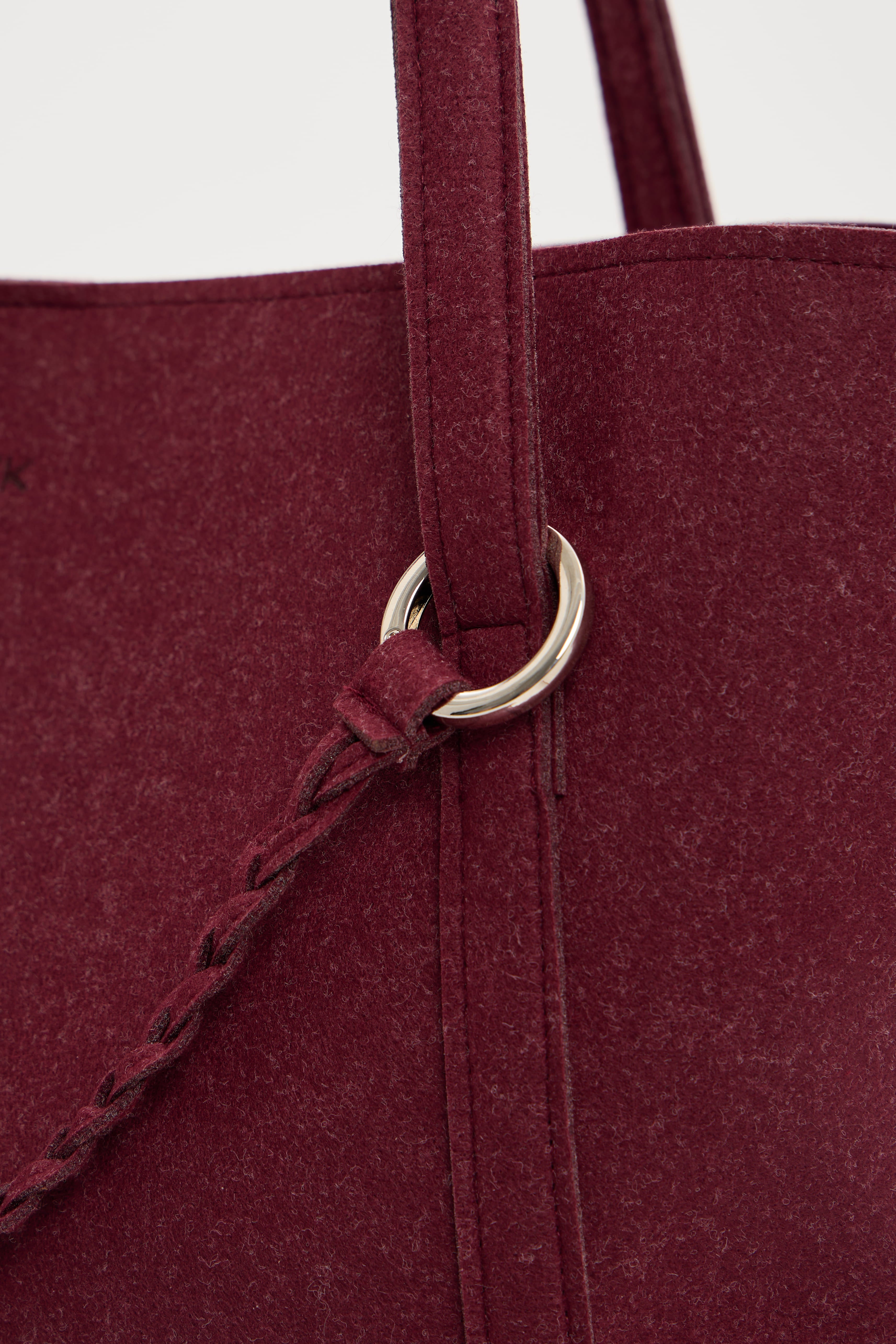 Close-up of a burgundy tote bag with a metal ring handle on a white background