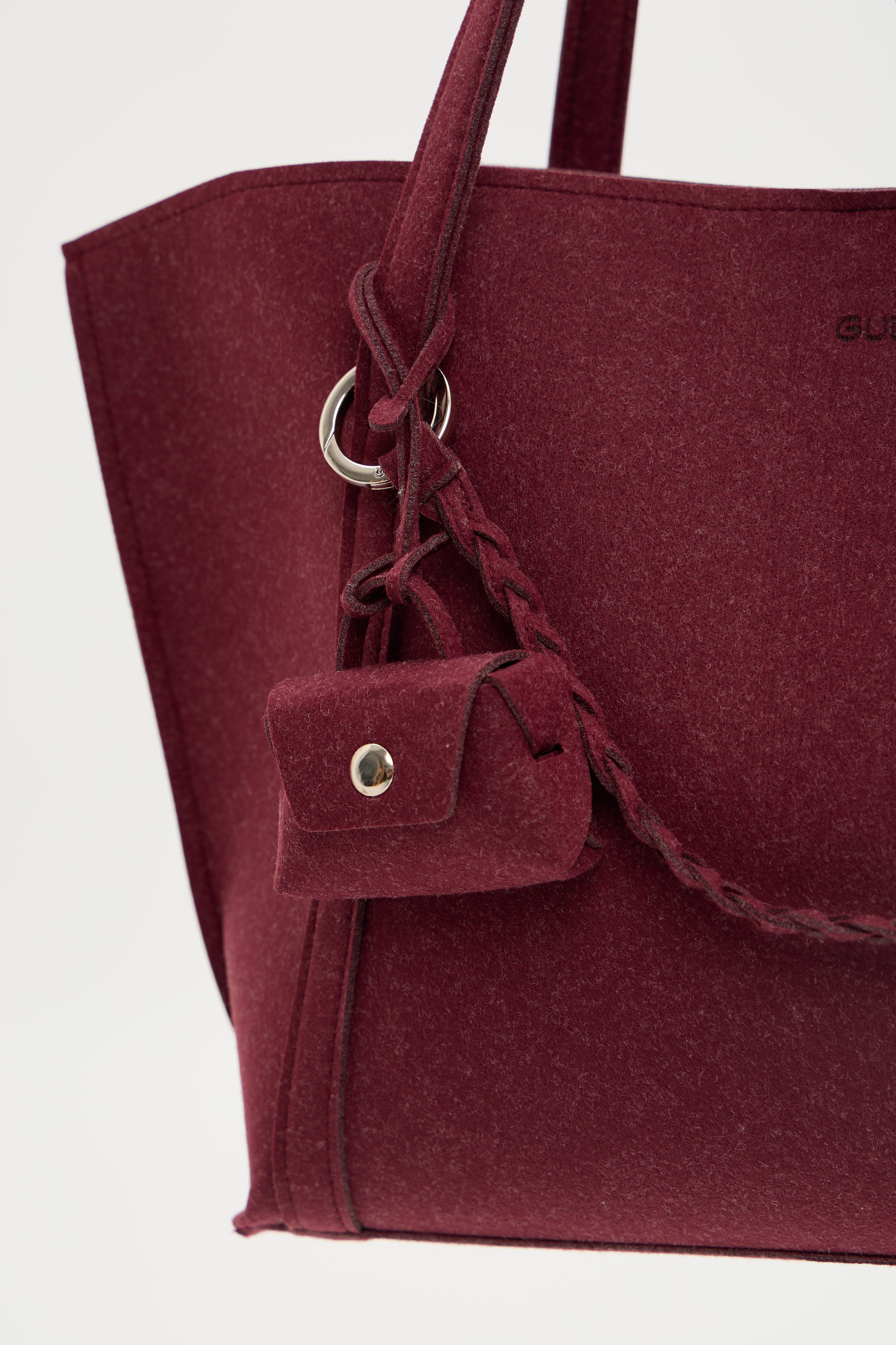 Close-up of a burgundy tote bag with a small pouch attached on a light gray background