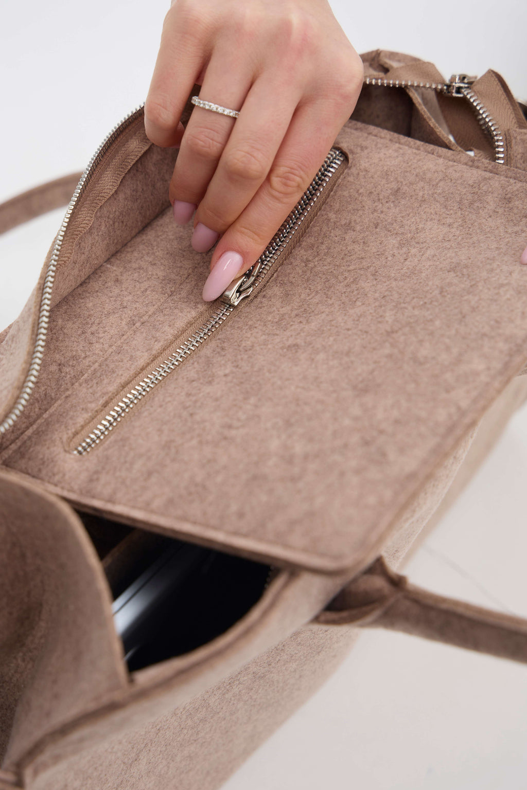 Close-up of a hand opening a beige handbag with a zipper.
