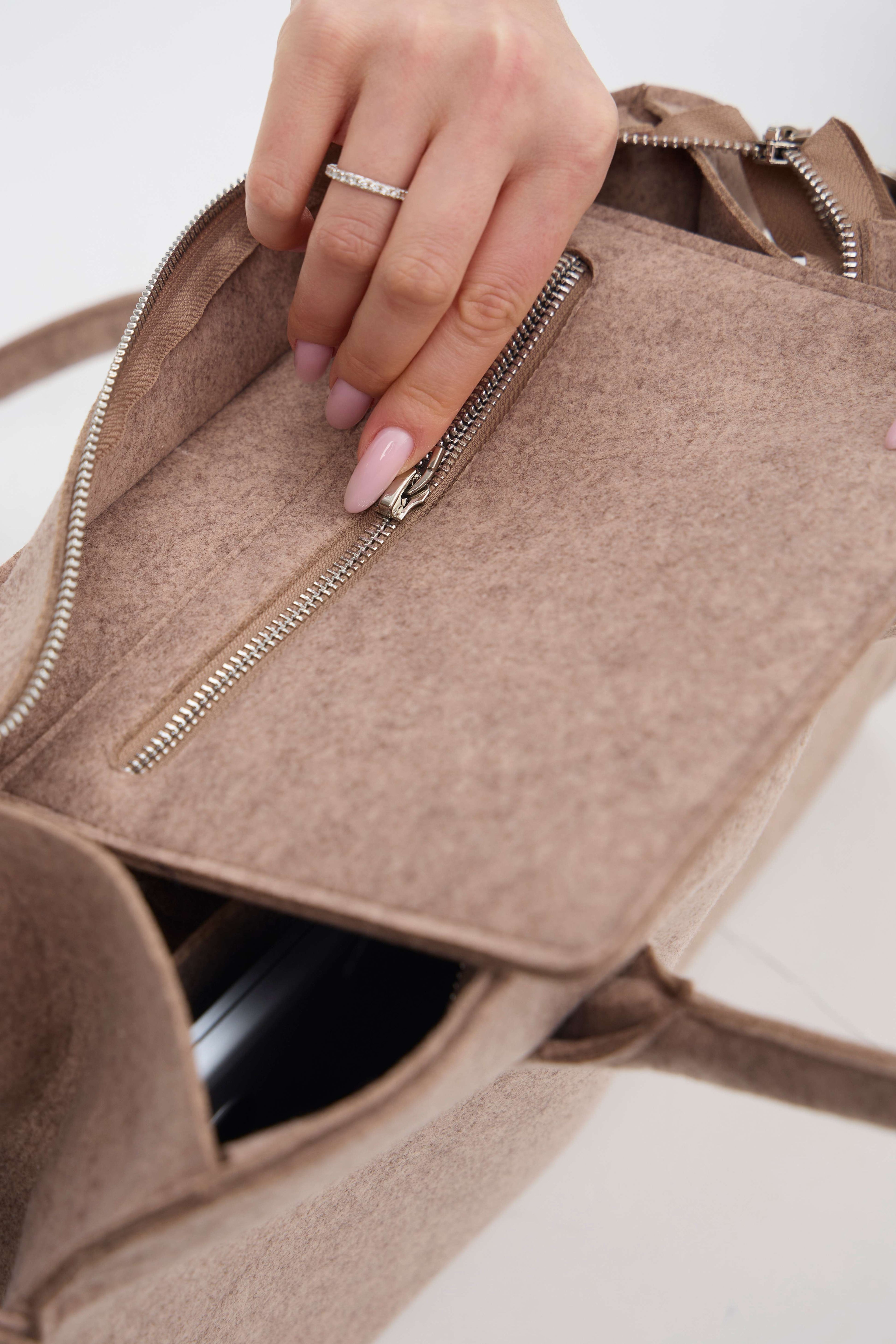 Close-up of a hand opening a beige handbag with a zipper.
