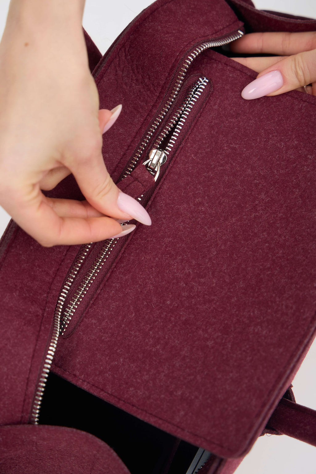 Close-up of a maroon backpack with a hand opening the zipper.