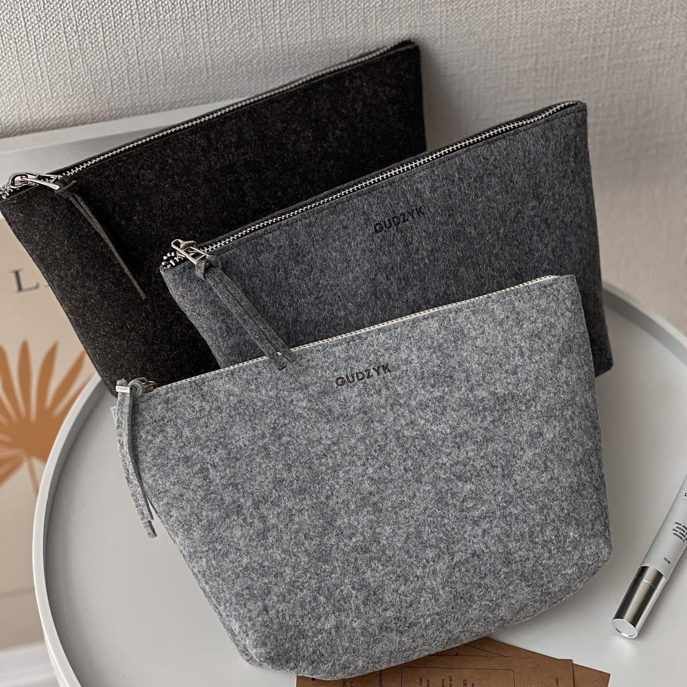 Gray and black felt pouches with 'GUDZYK' branding on a white surface.
