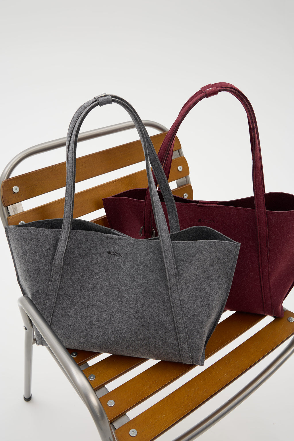 Gray and burgundy tote bags on a wooden chair with a white background