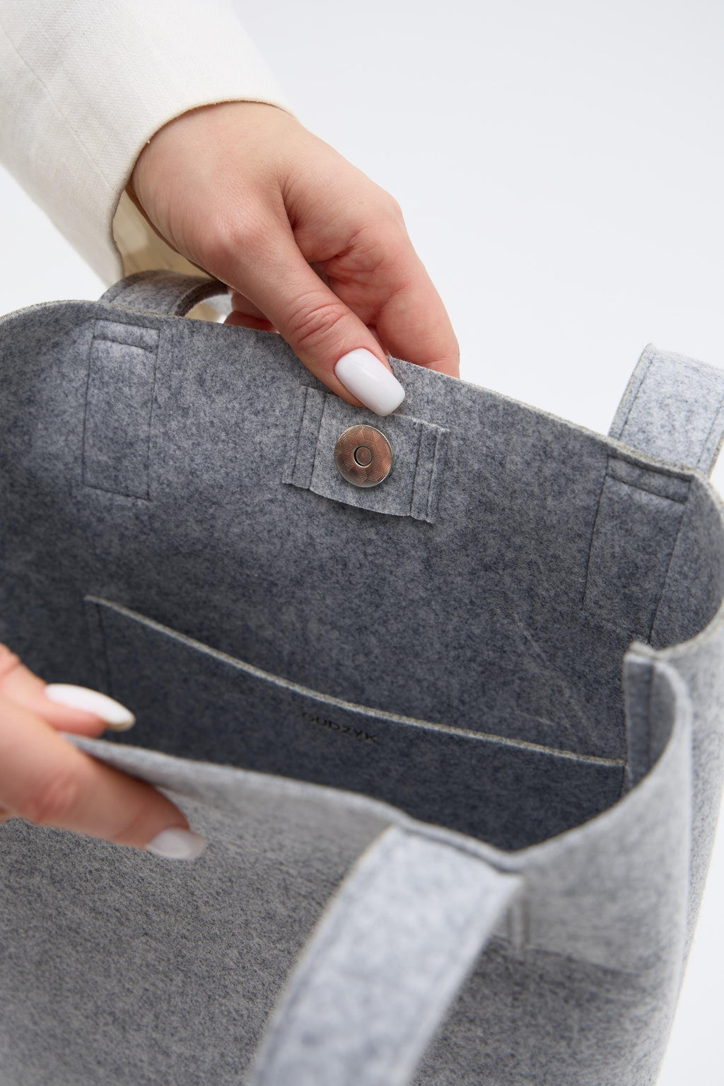 Gray felt bag held by a hand with white nail polish on a light gray background