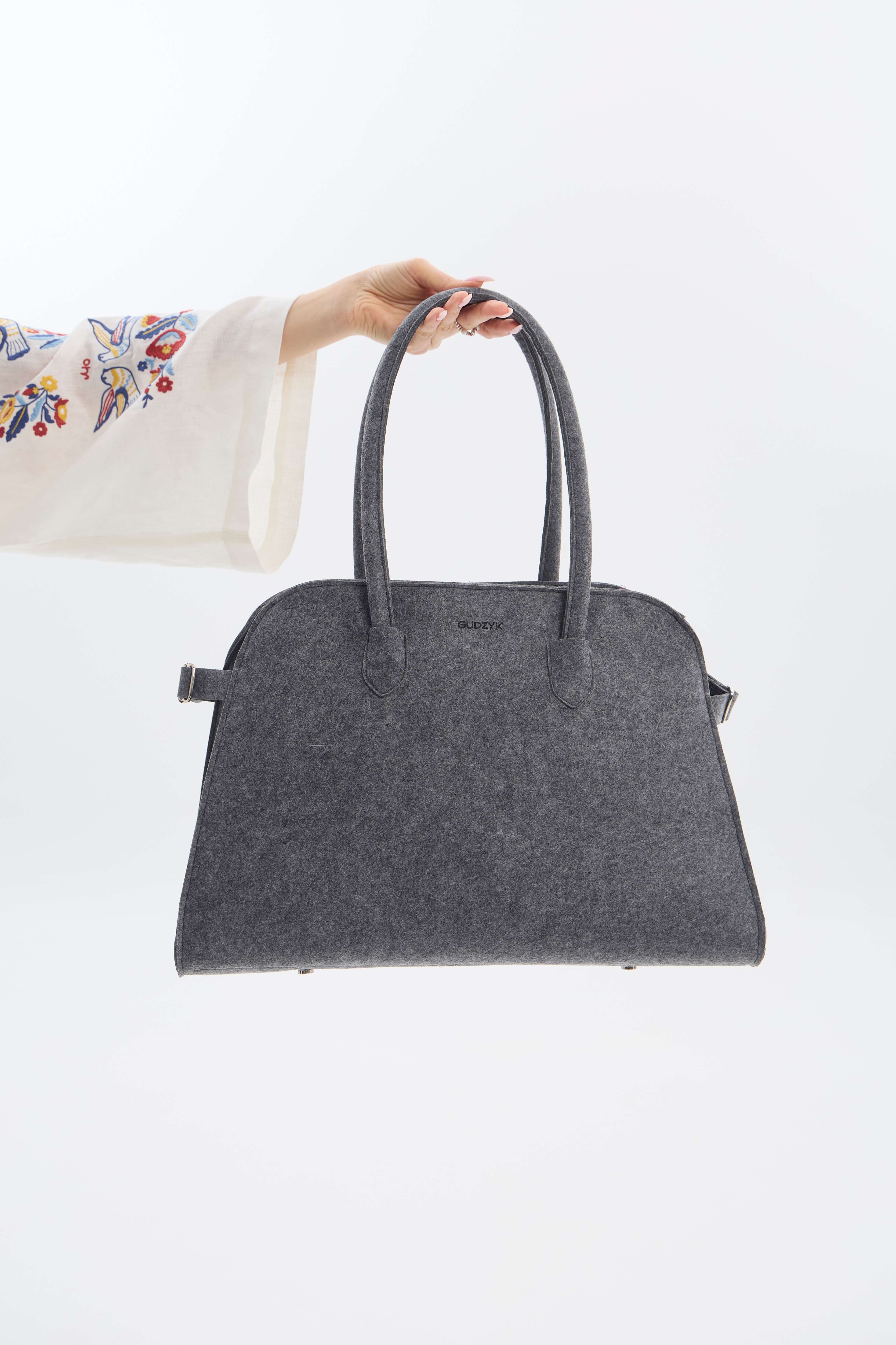 Gray handbag held by a hand against a white background