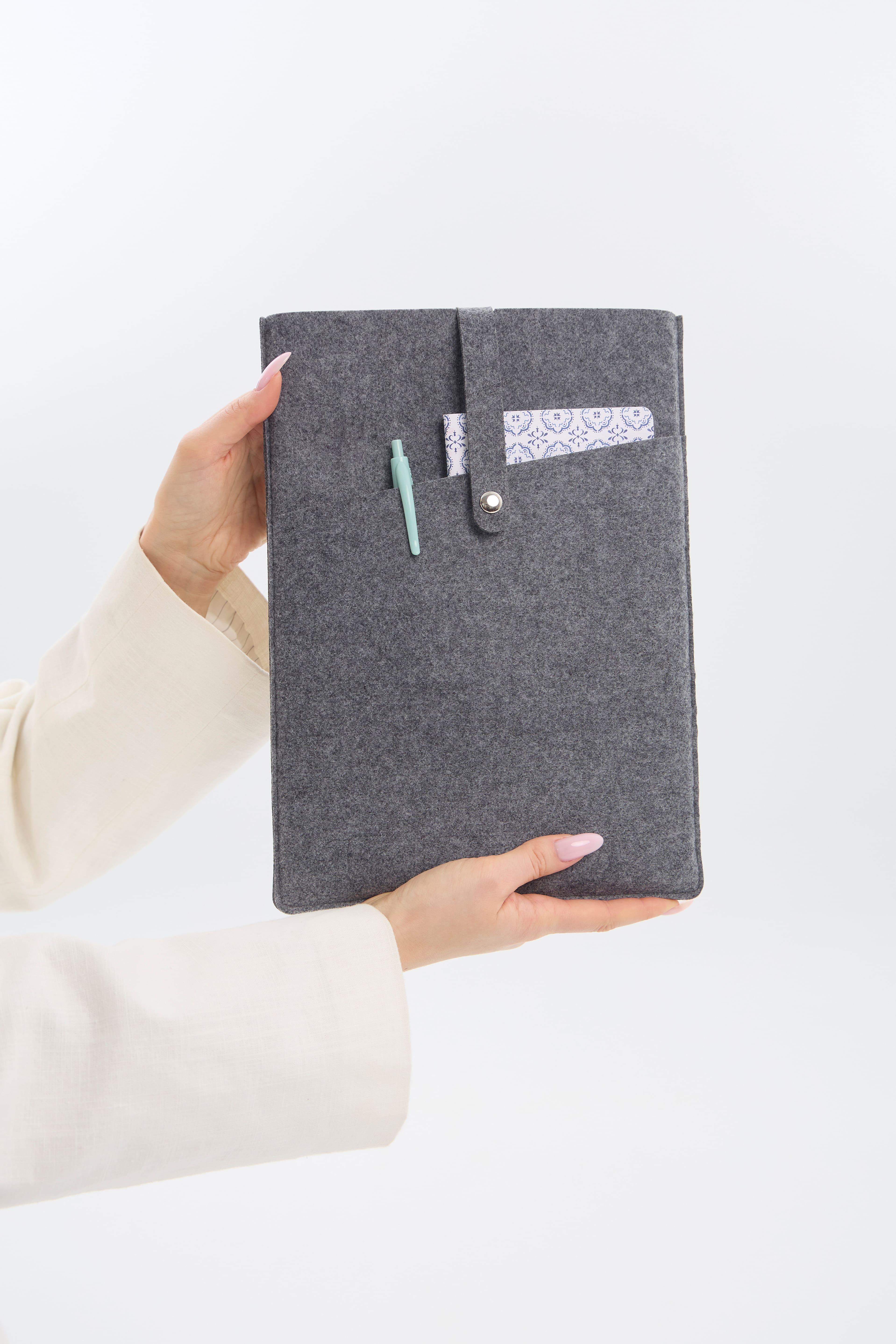 Person holding a gray felt laptop case with  pocket on a white background