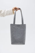 Gray tote bag held by a person against a white background