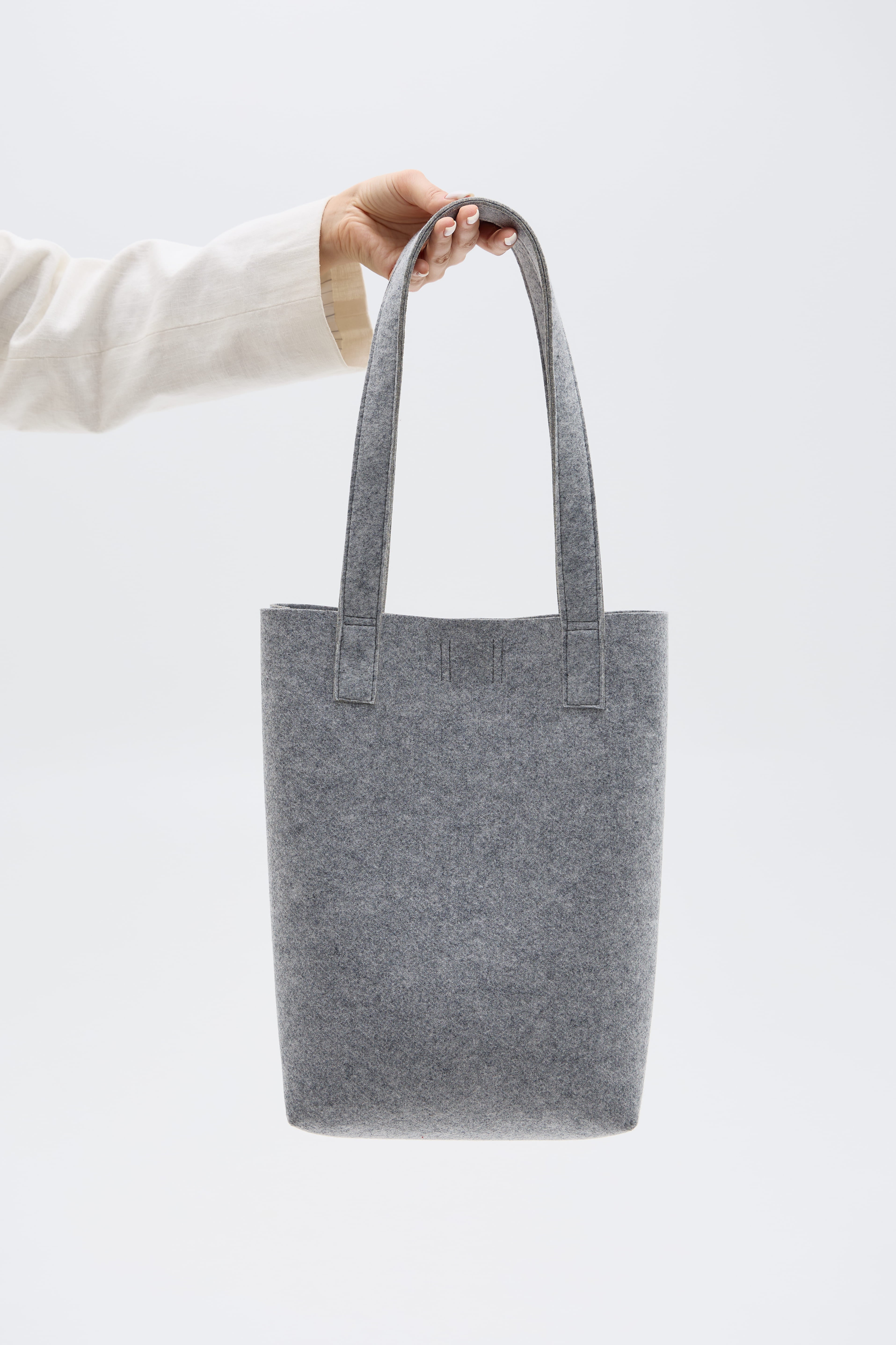 Gray tote bag held by a person against a white background