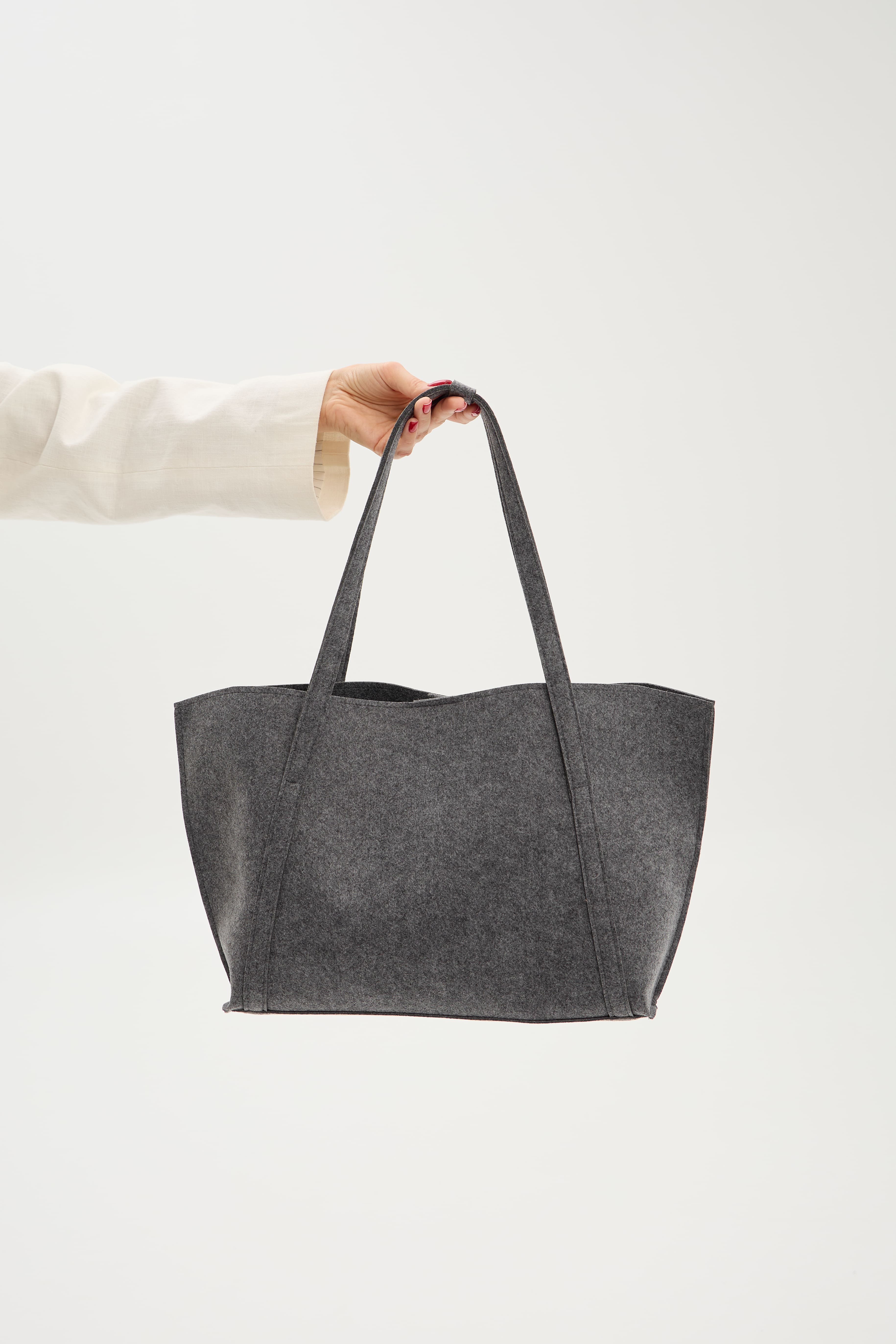 Gray tote bag held by a person against a white background