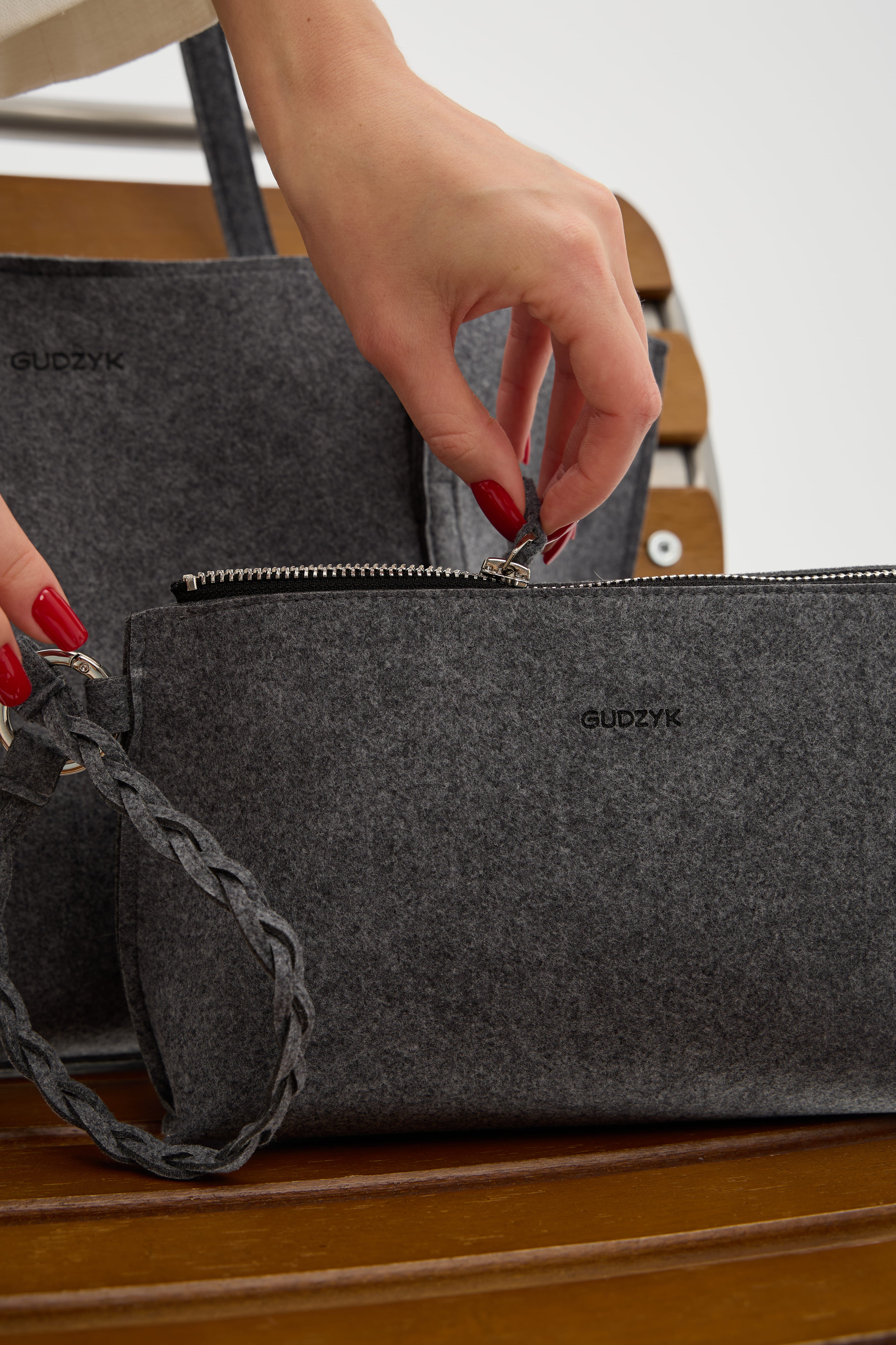 Gray makeup bag with 'GUDZYK' branding held by a hand on a wooden surface.