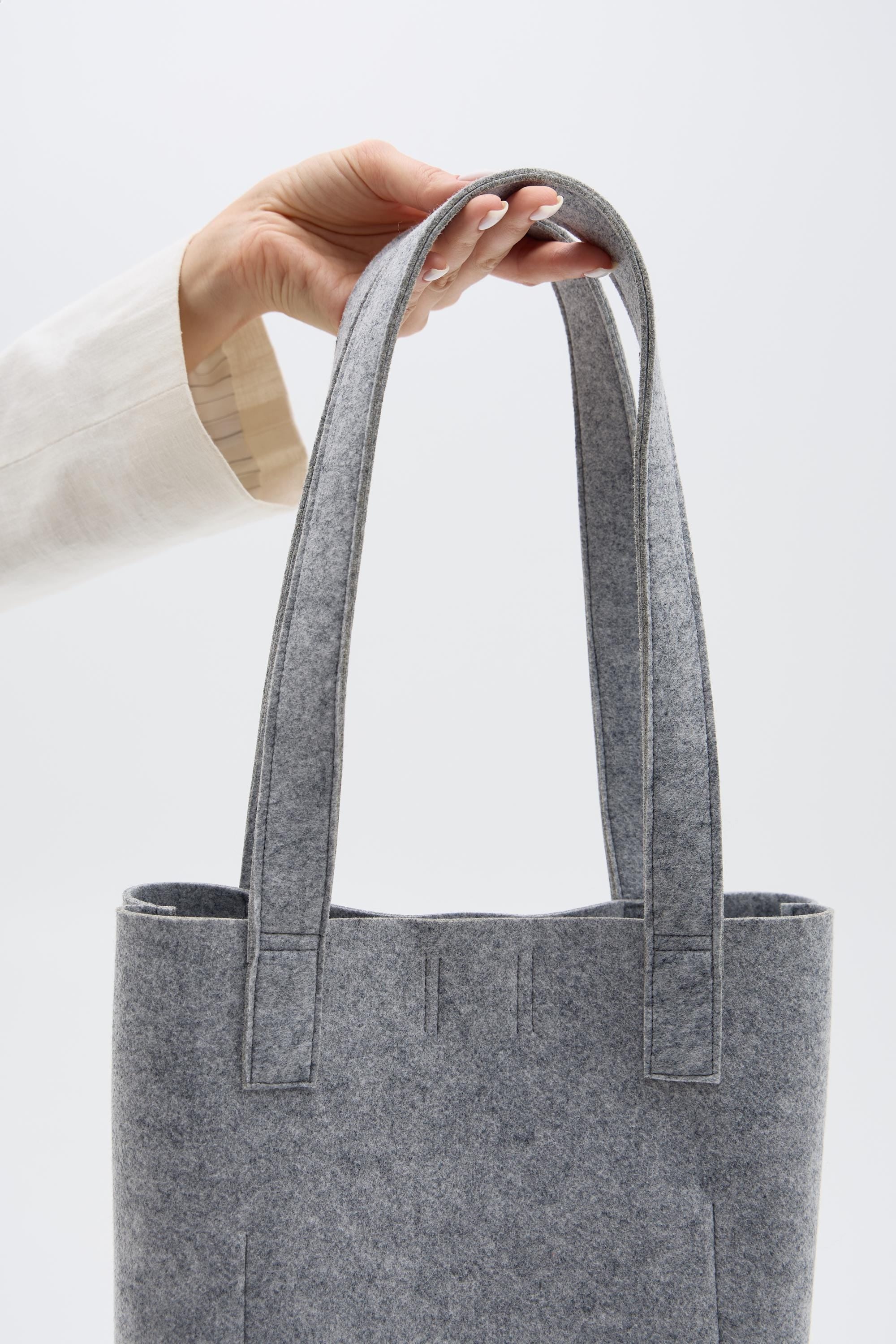 Silver tote bag held by a hand against a white background