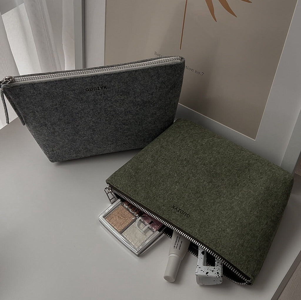 Green and grey felt cosmetic bags with makeup items on a light surface